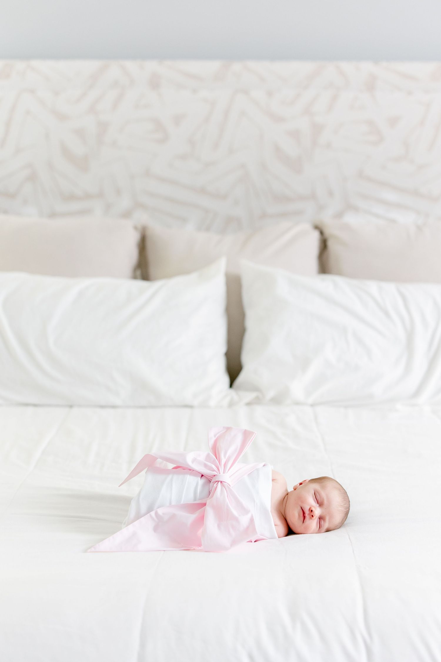 A sleeping newborn in pink wrap lies on white bedding.
