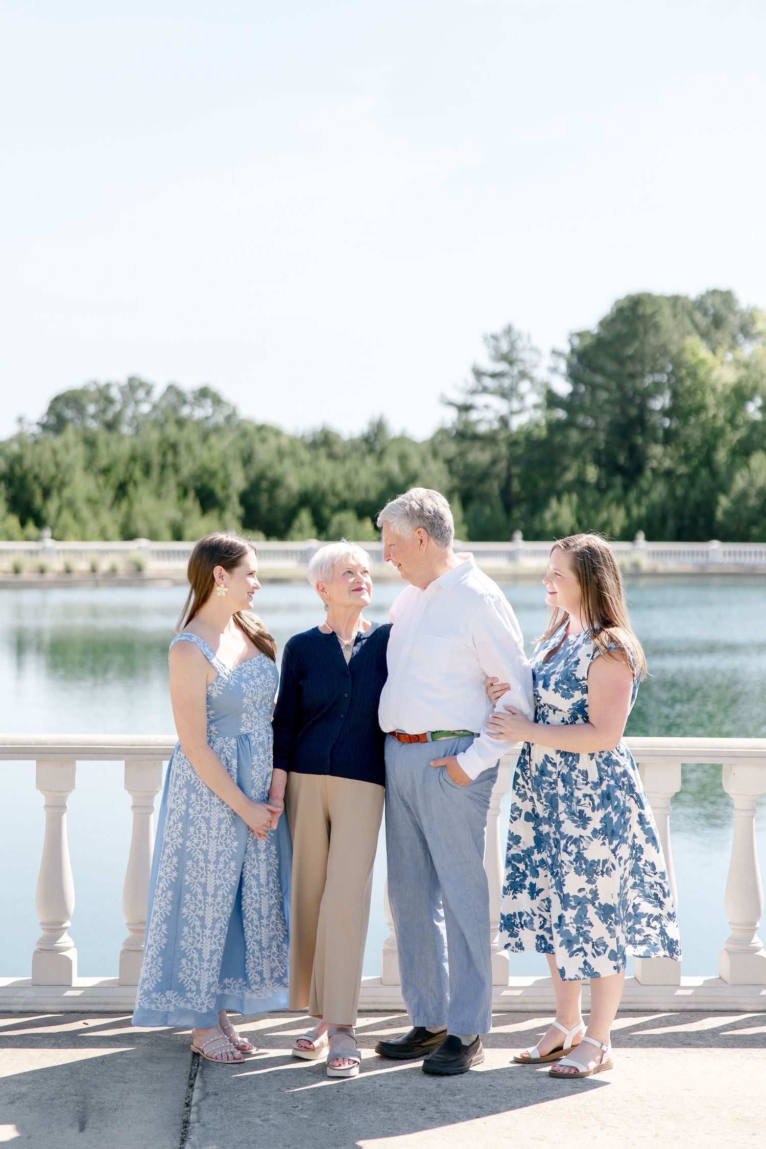Family enjoying a sunny day together on a stone balcony overlooking a serene lake surrounded by trees.