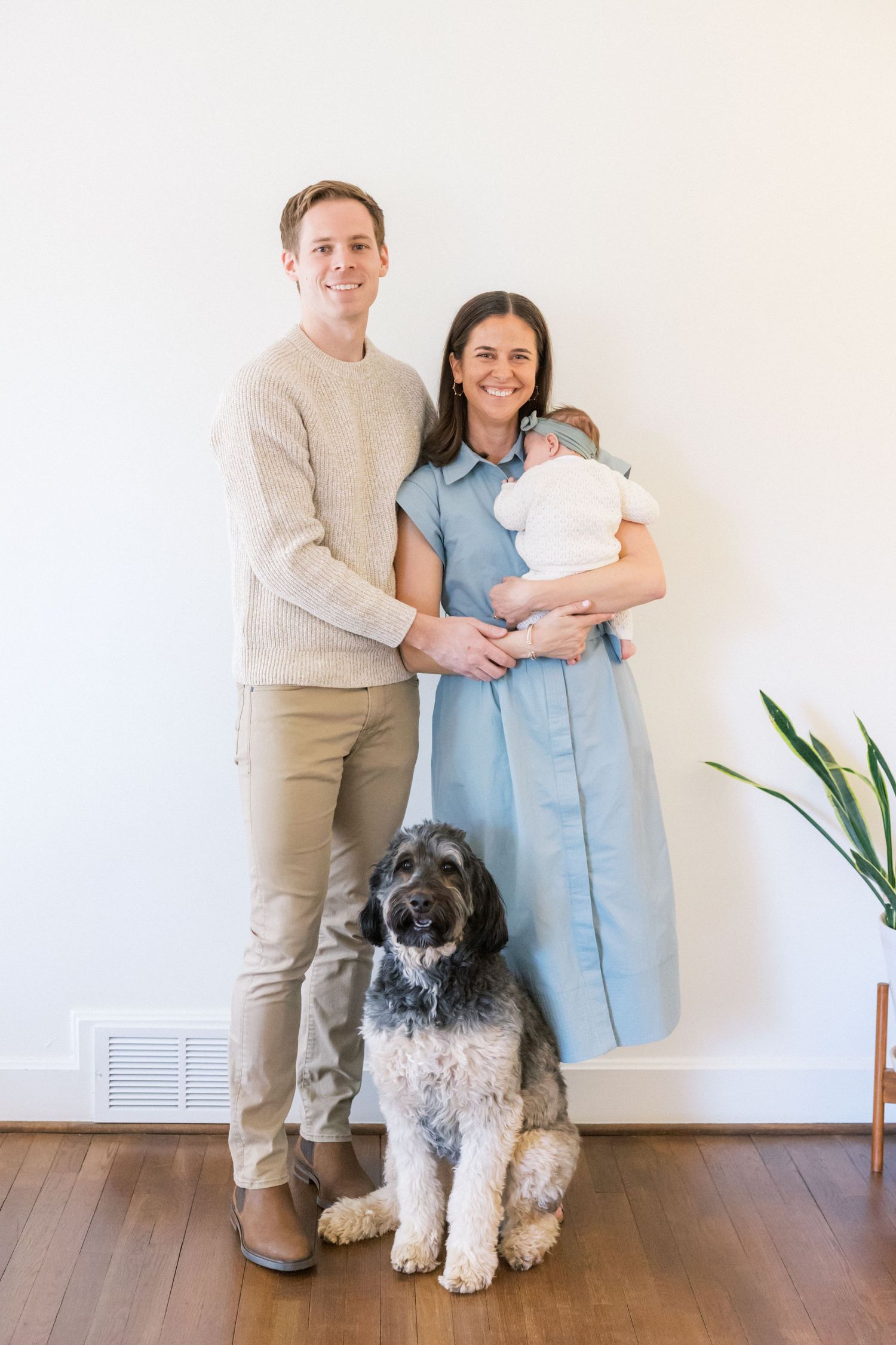 Family portrait with baby, parents, and their fluffy black and white dog against white wall.