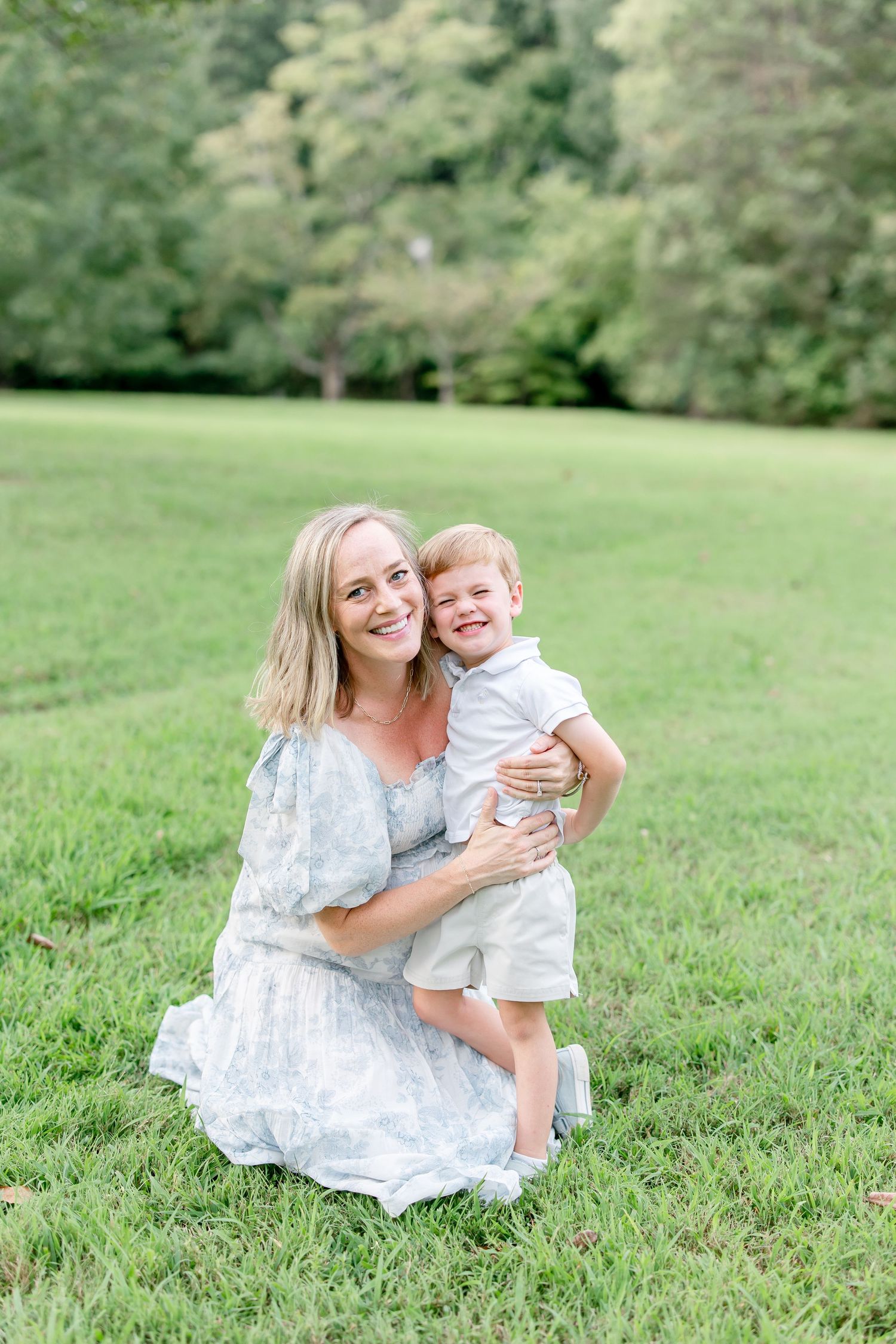 A tender moment between parent and child as they sit and laugh together in a sunny green field on a summer day.