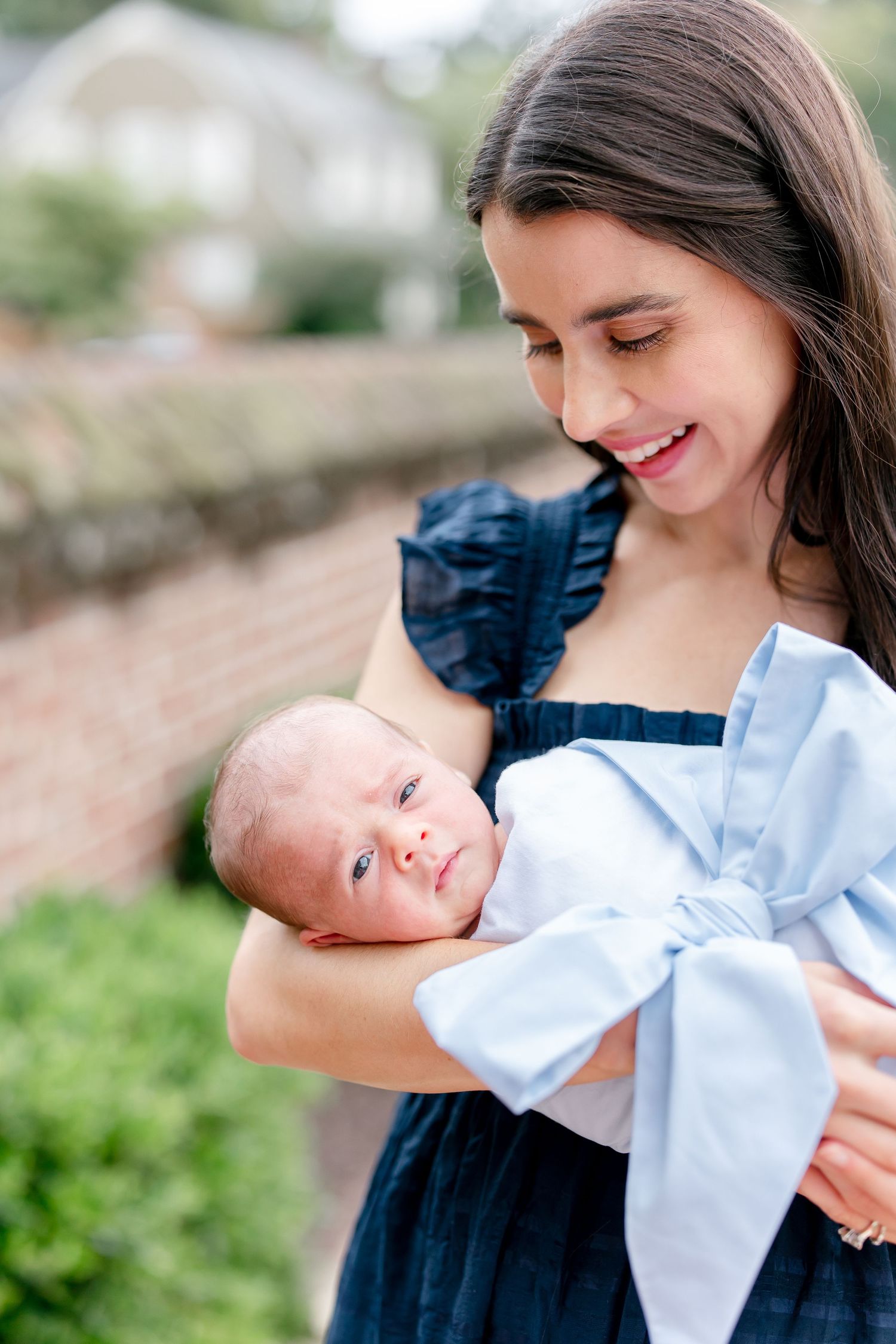 Outdoor family portrait series showing tender moments with newborn baby in white outfit.