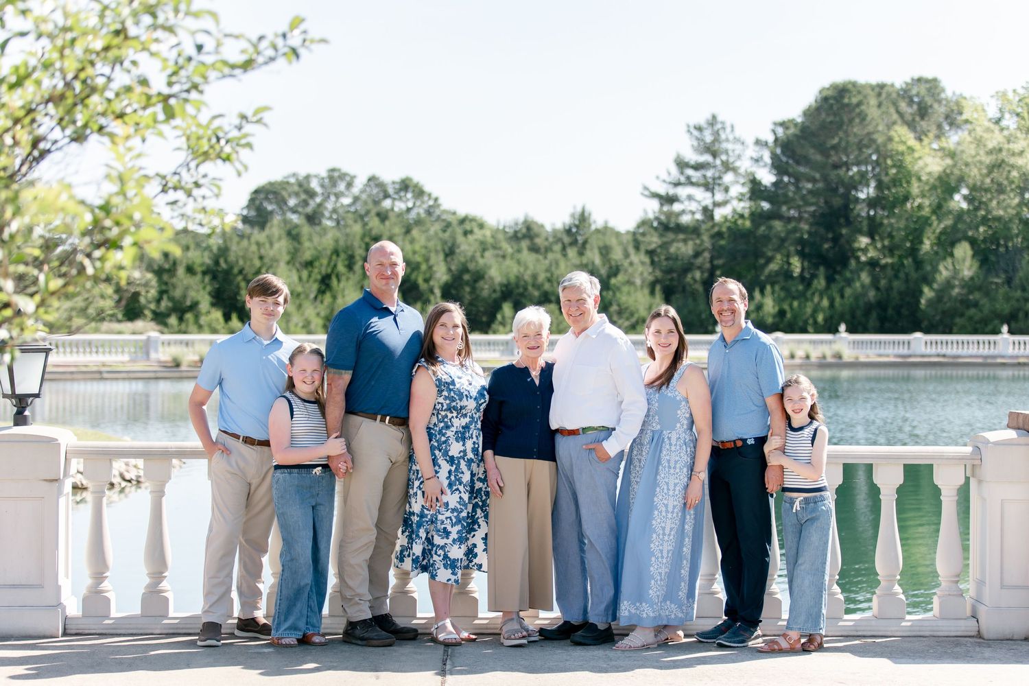 A group stands together on a white balcony overlooking a serene lake on a sunny summer day.