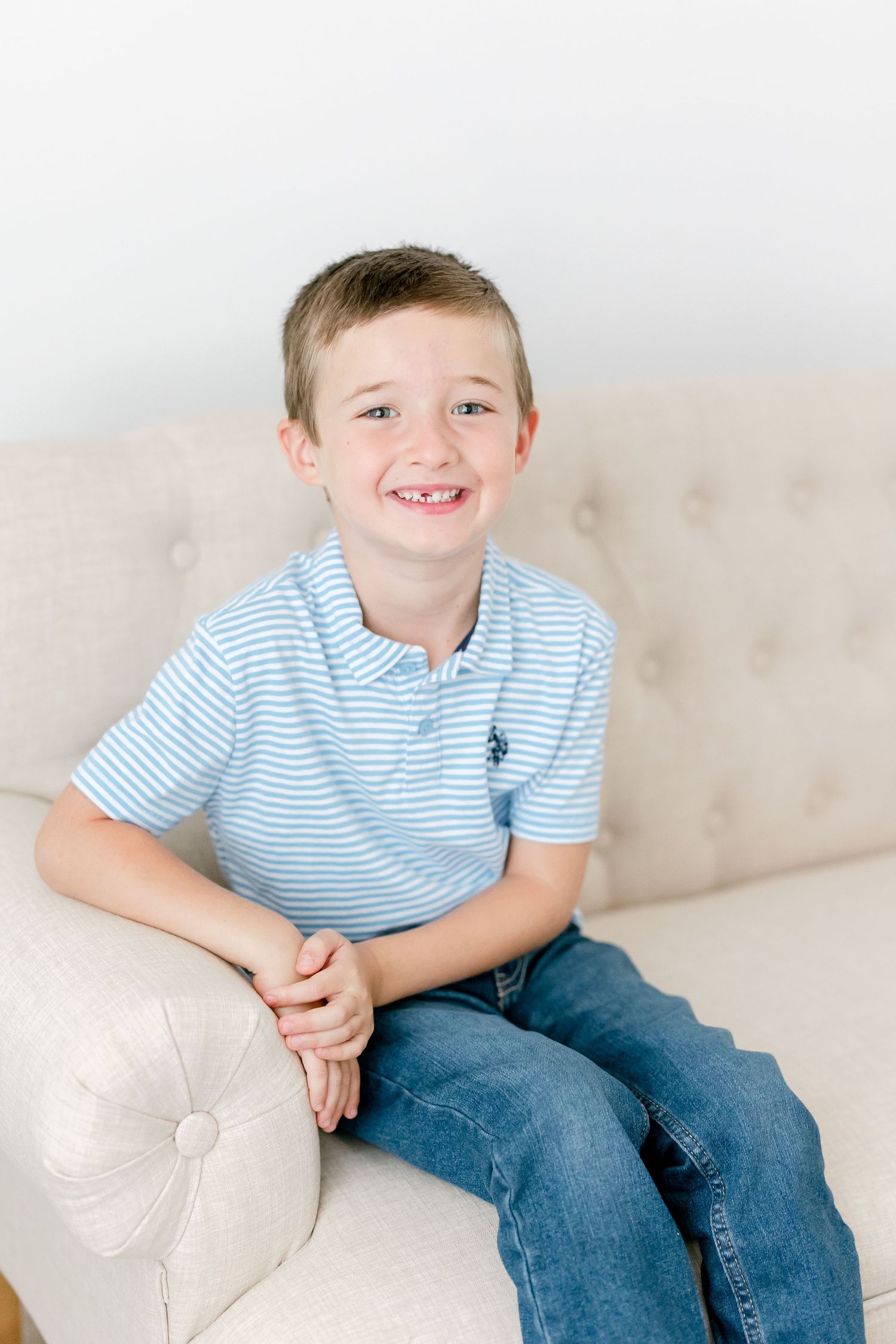 Child relaxing on a light-colored couch wearing blue striped shirt and jeans.