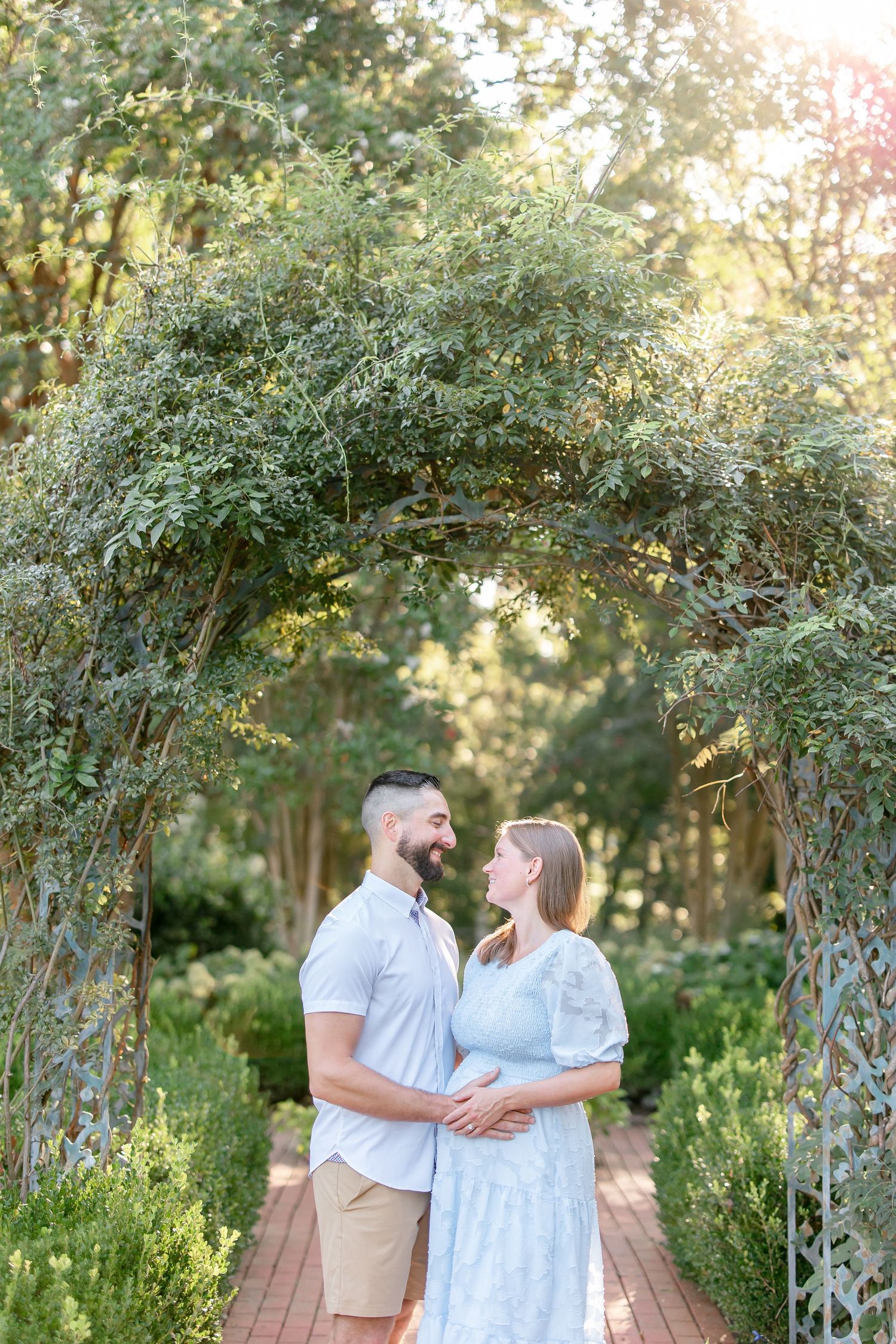 Romantic couple poses beneath a vine-covered garden arch during a summer photo session.