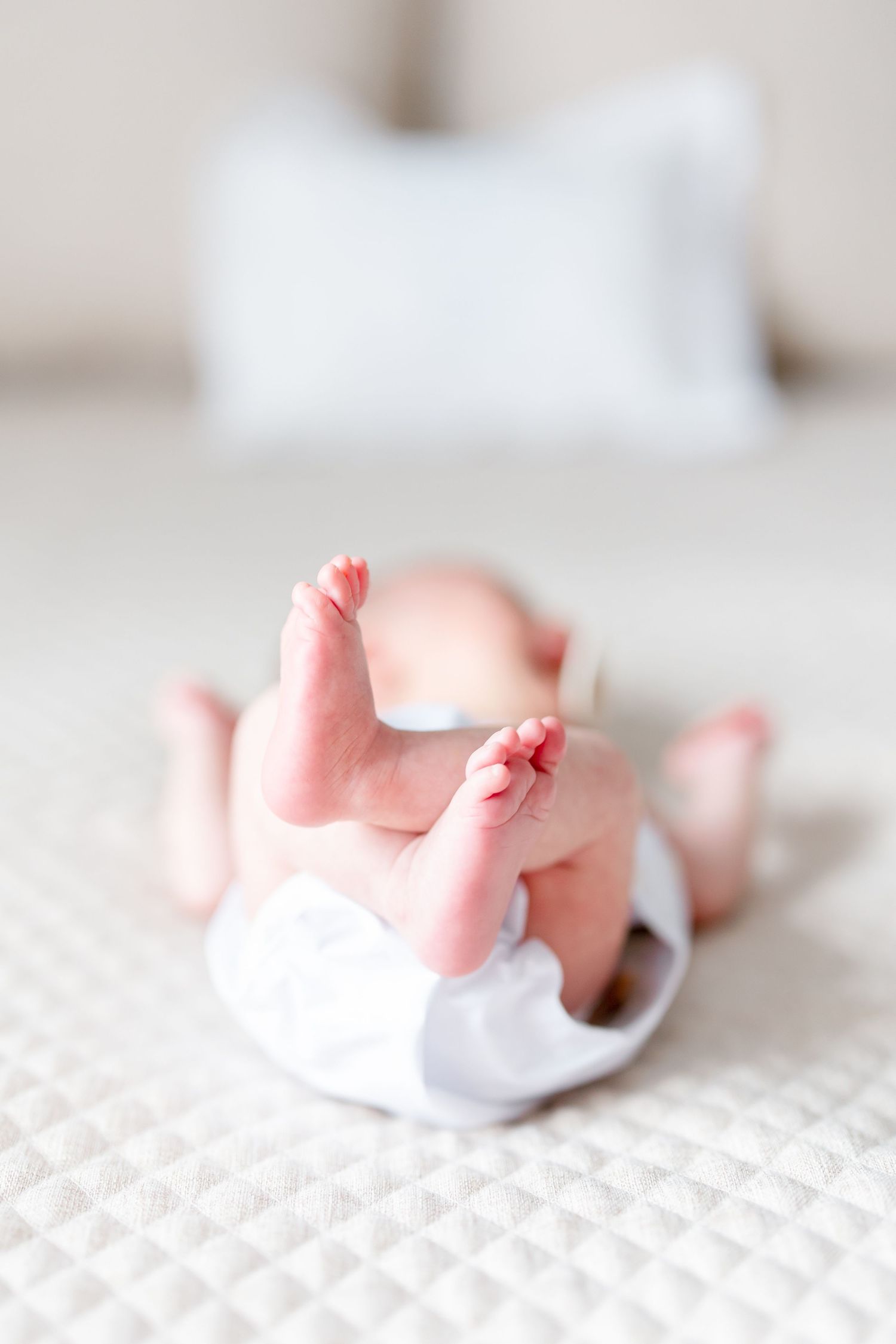 Pink baby feet and legs peeking out from white cotton fabric against a white textured background.