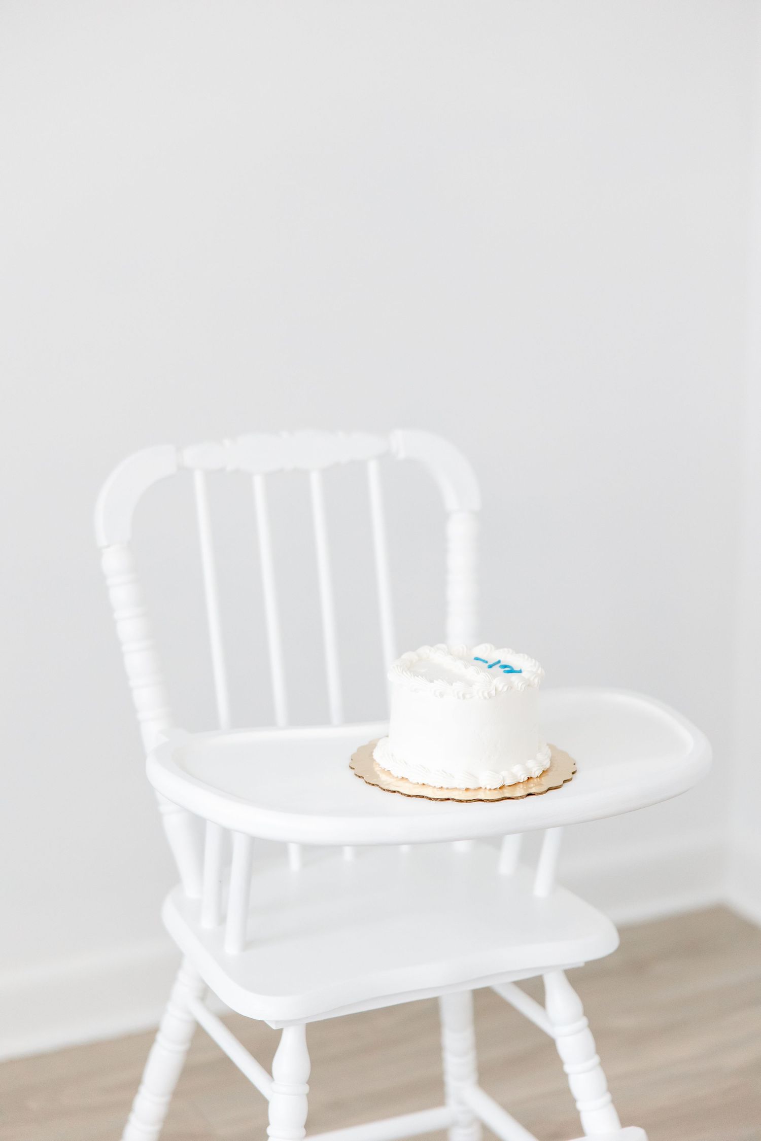 White wooden high chair with a plate sitting on top against light neutral background.