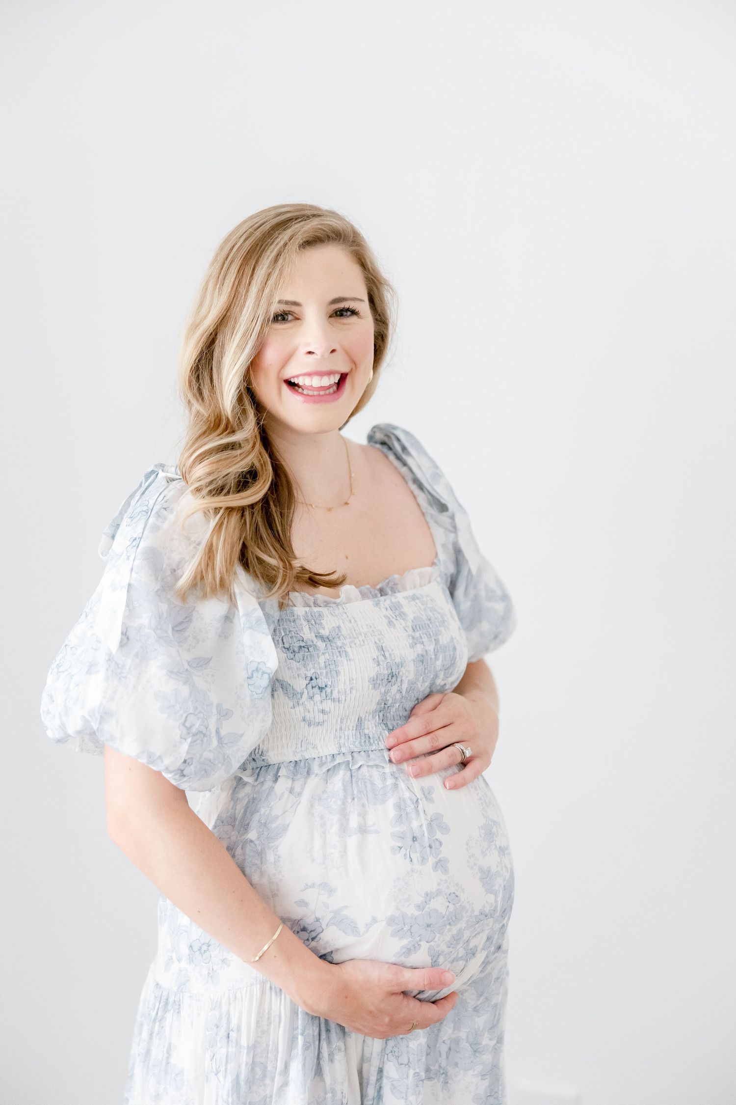 A beautiful maternity portrait showing a blue and white floral dress against a light background.