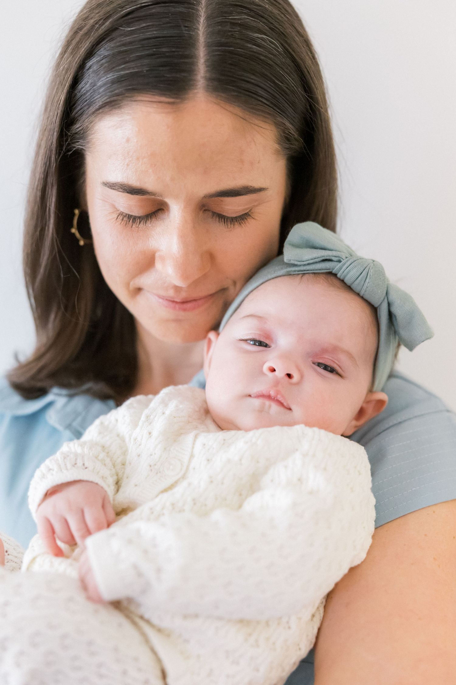 Baby in cream sweater and mint bow headband rests peacefully while being held.