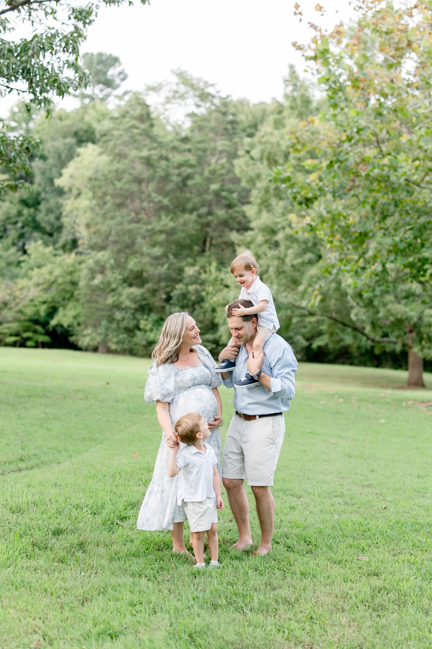 A family stands together and laughs while enjoying a sunny afternoon in a park setting.