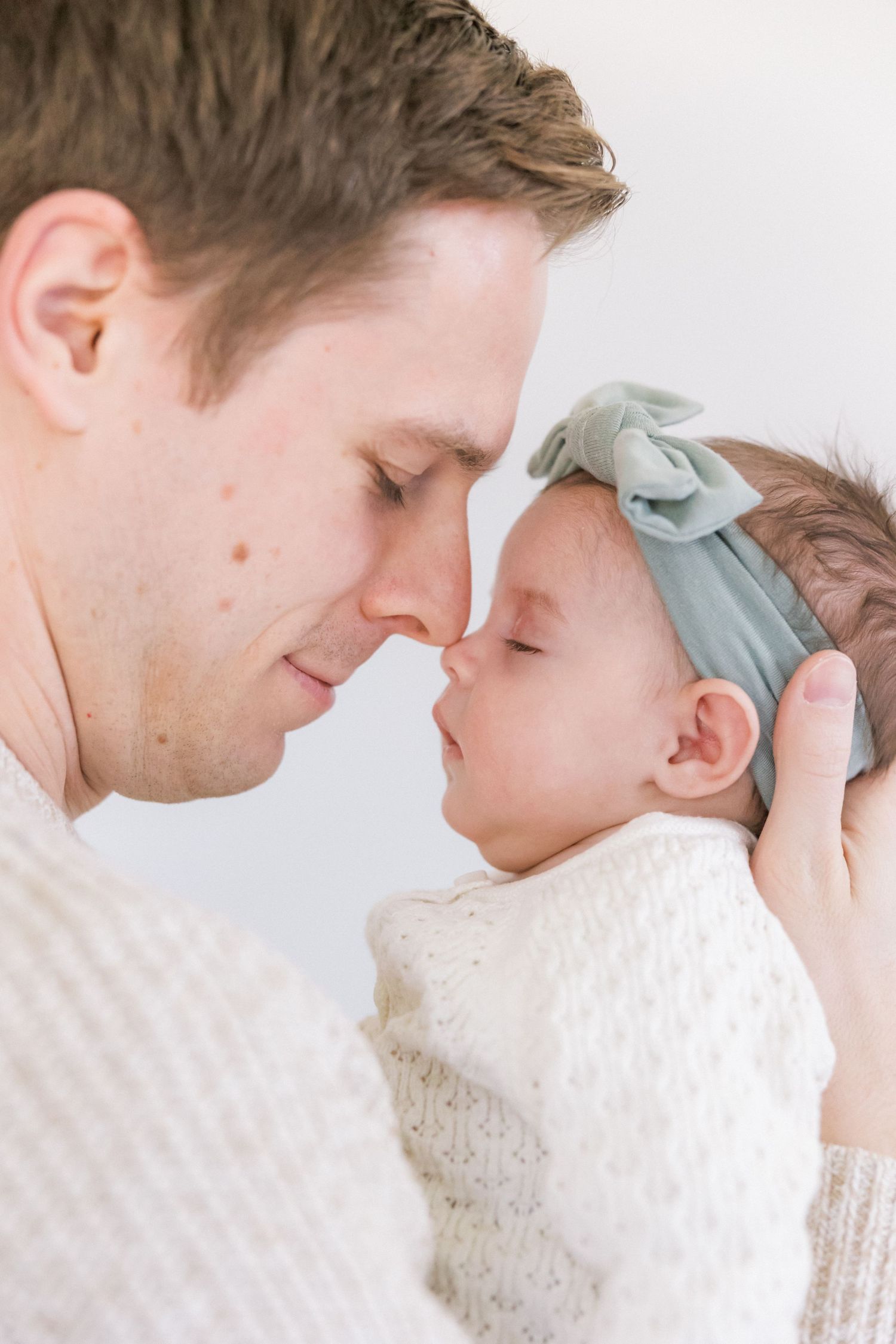 Sweet moment with baby in white knit outfit and mint headband being cradled close.