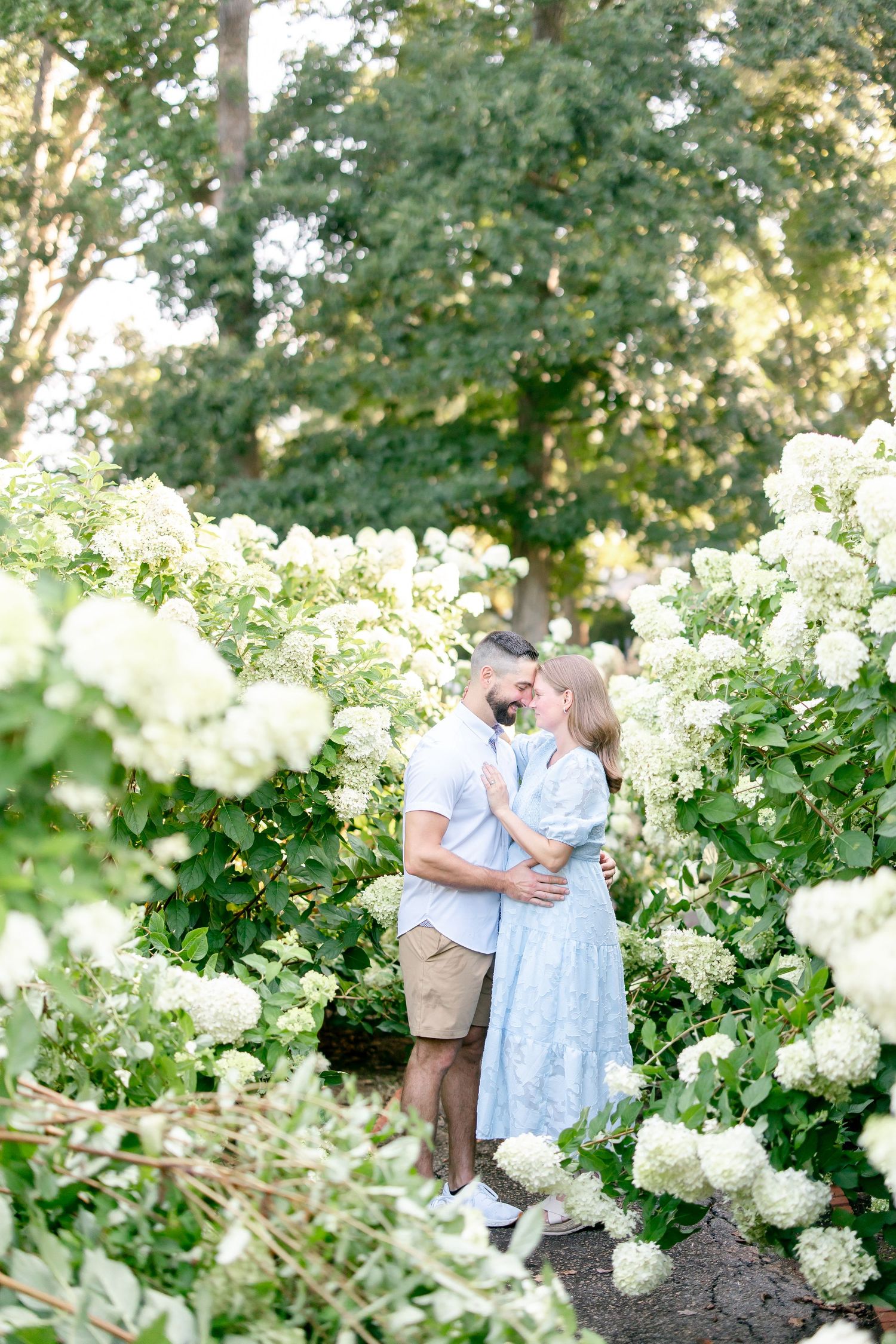 A romantic moment captured in a garden setting surrounded by blooming white hydrangea flowers and lush greenery.