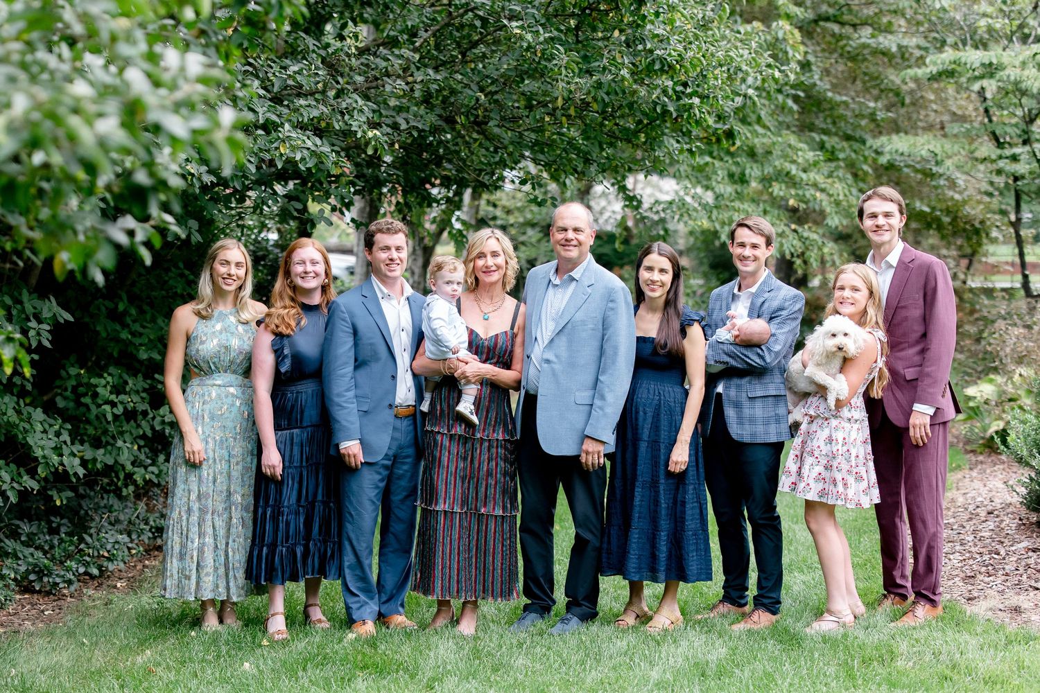 Wedding party stands together in an outdoor garden setting wearing blue and purple coordinated dresses and suits.