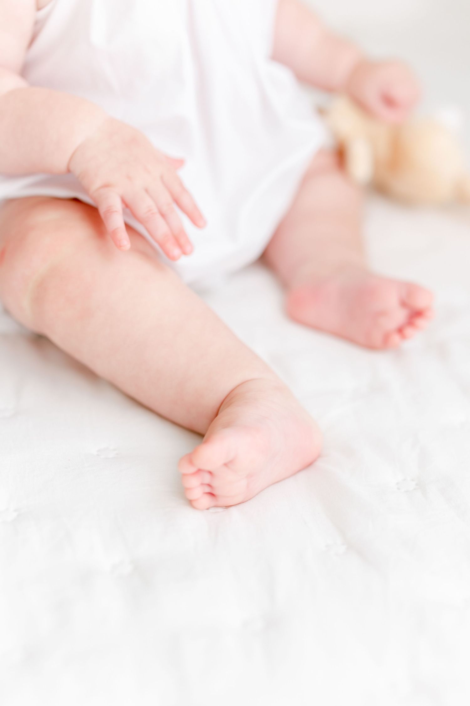 Close up of tiny baby feet and legs against white bedding in soft natural light.