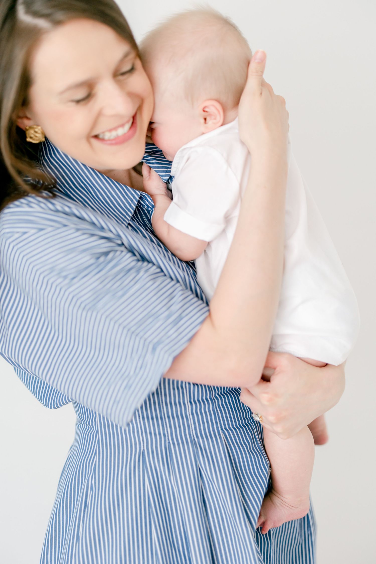 Adult holding and playfully interacting with smiling baby in white clothing.