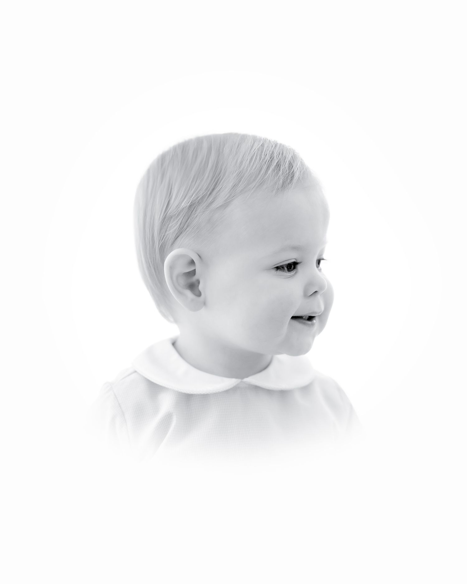 Black and white portrait of a smiling baby in profile wearing a white top.