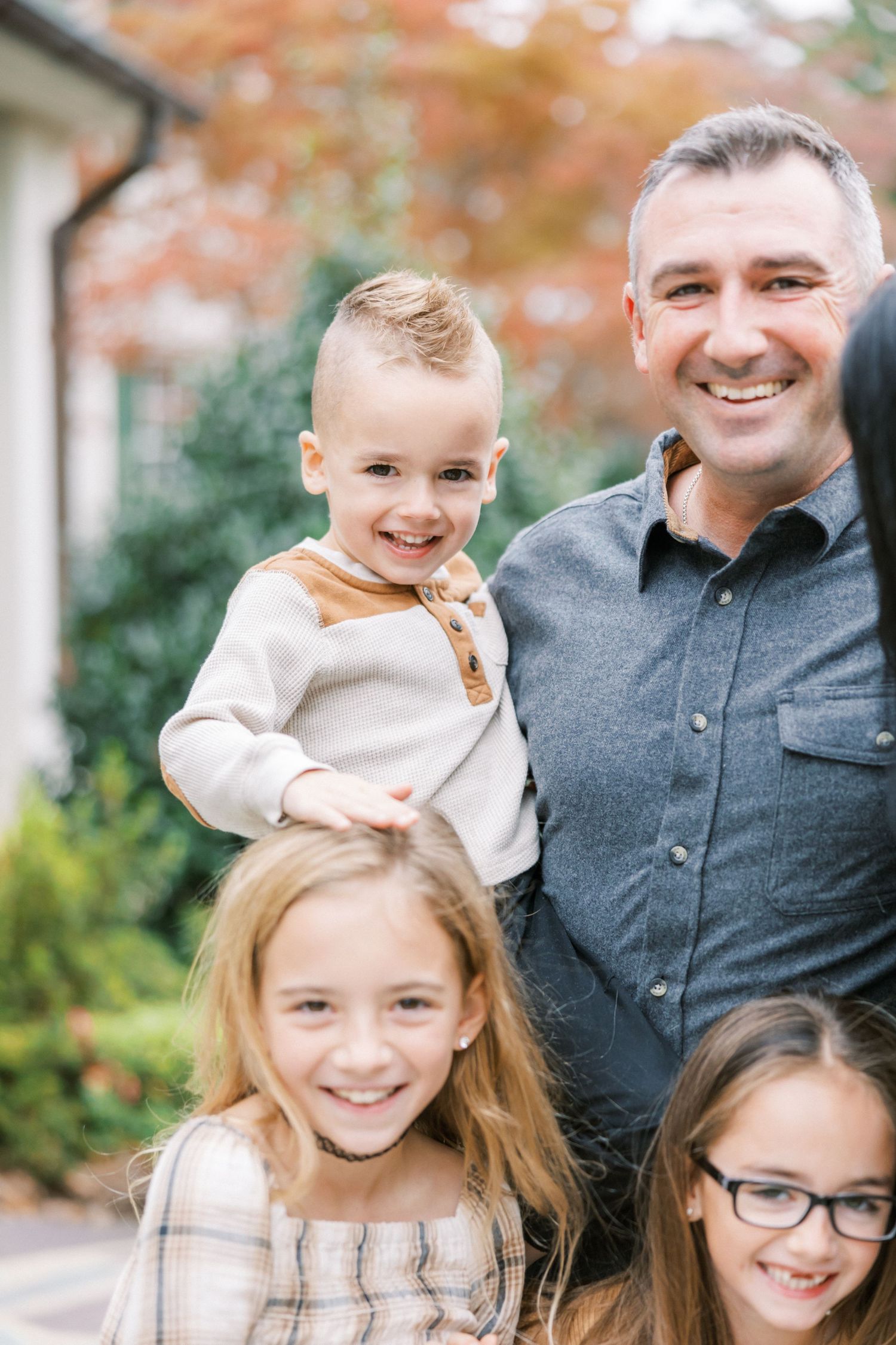 A happy family poses together outdoors in autumn with fall foliage visible in the background.