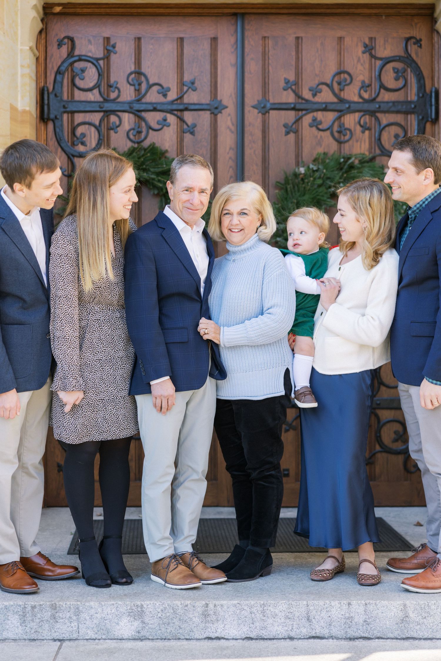 A family group stands together on stone steps in front of ornate wooden doors, wearing coordinated casual attire.