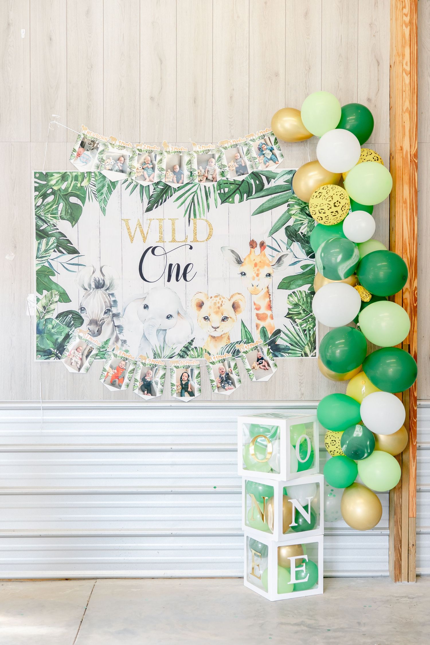 Green and white safari-themed birthday backdrop with balloon garland and decorative blocks.