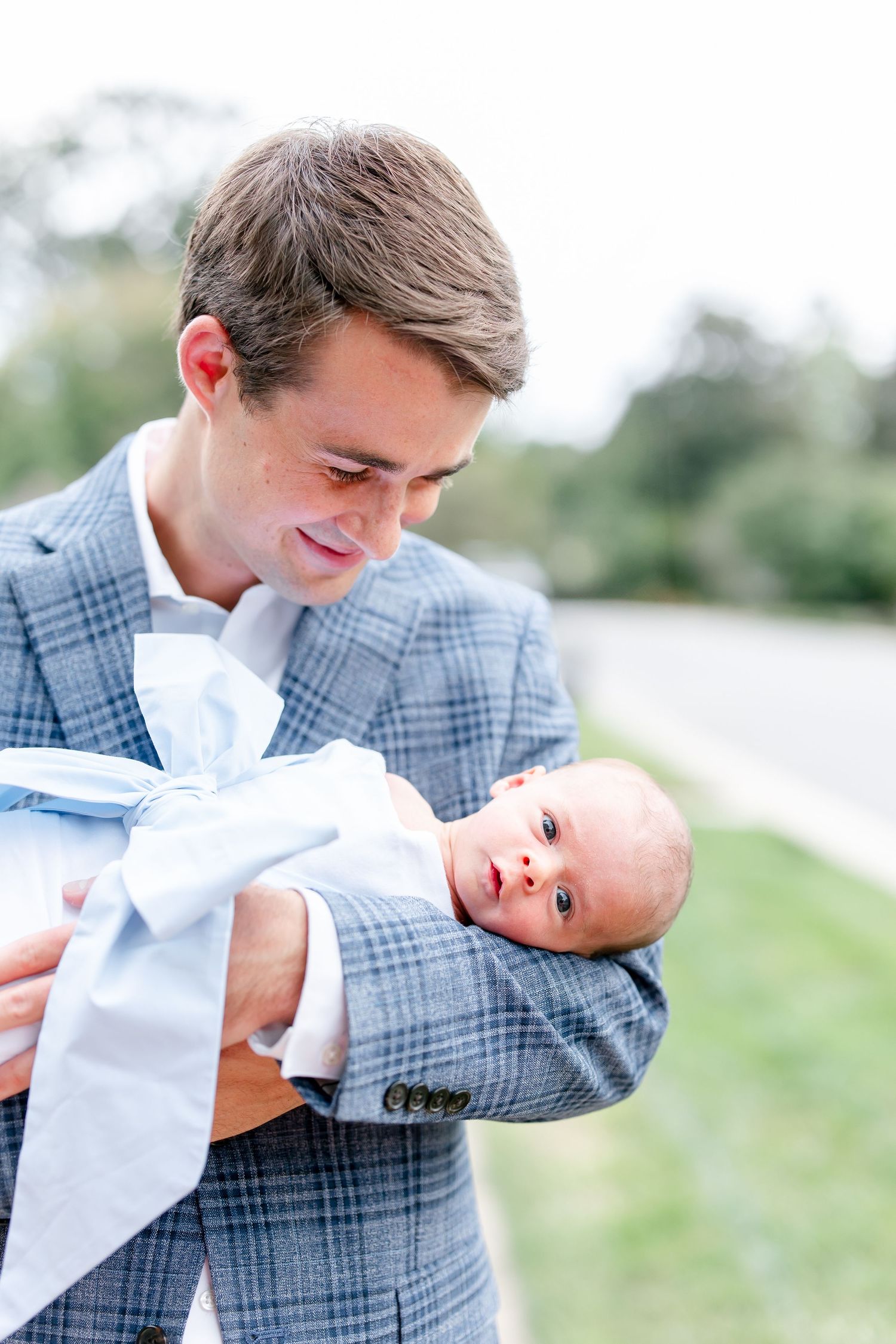 Man in plaid blazer tenderly holding newborn baby outdoors in sequence.