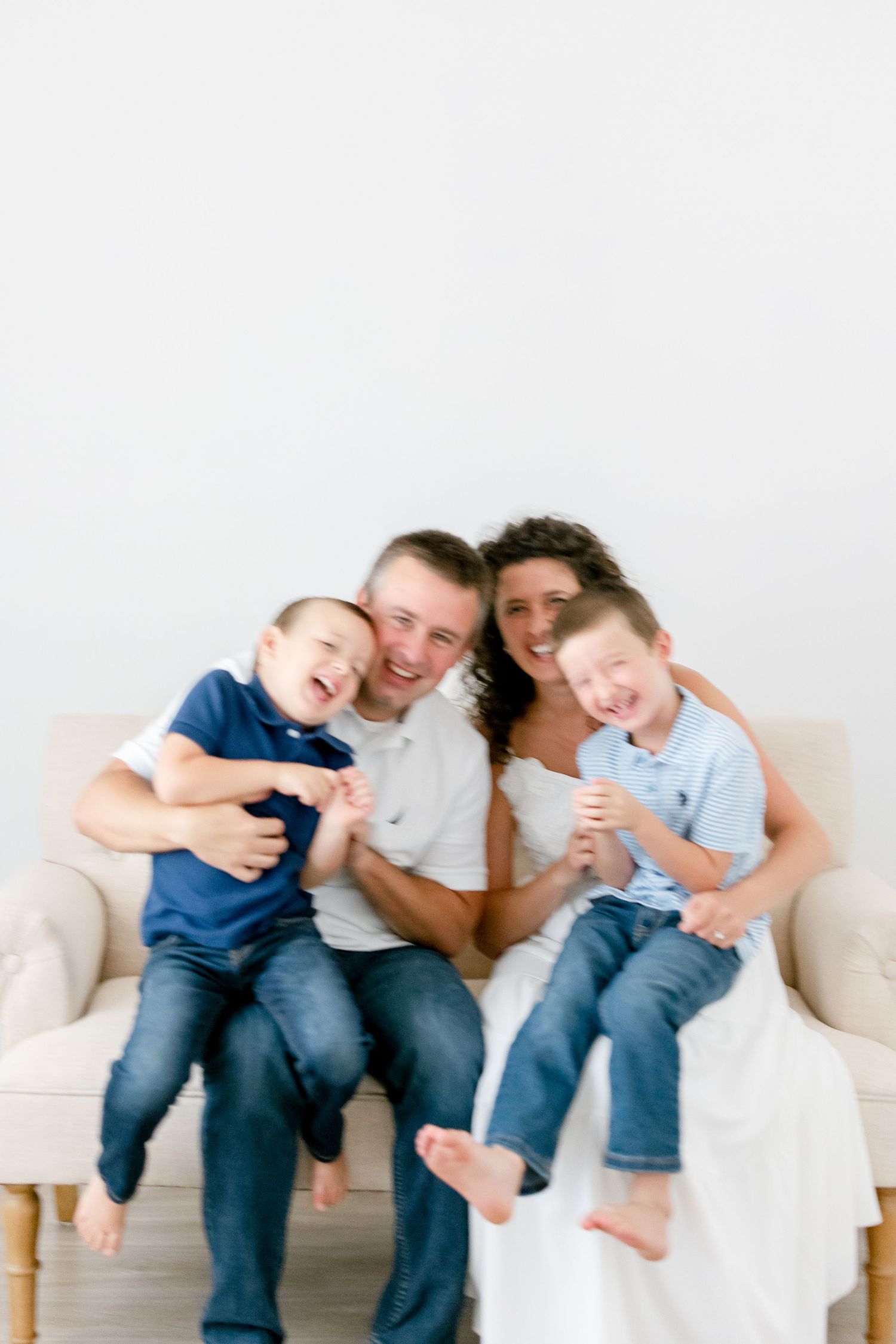 A family relaxes together on a white couch showing playful and candid expressions in matching casual outfits.