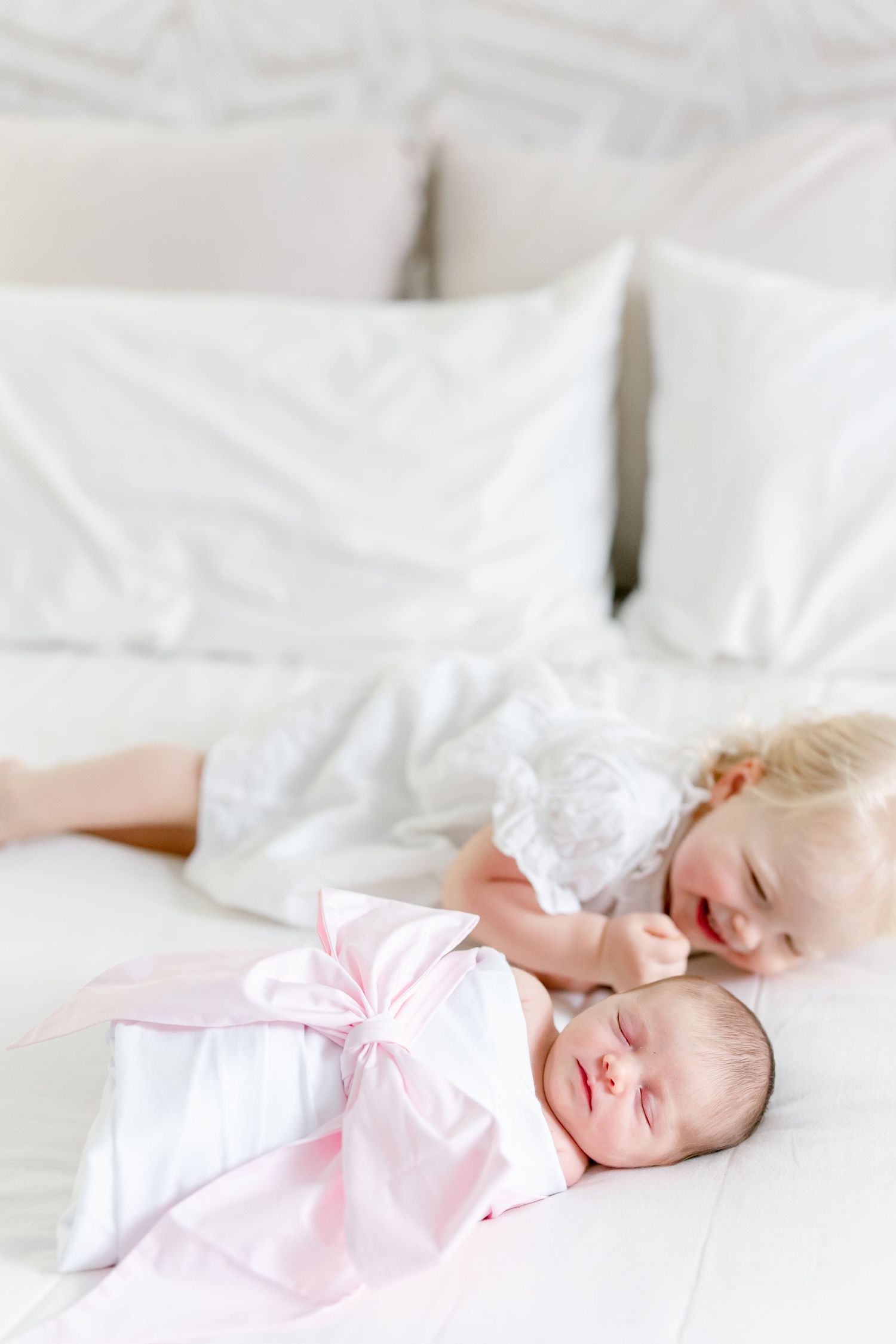 Newborn in pink outfit sleeps soundly on white linens.
