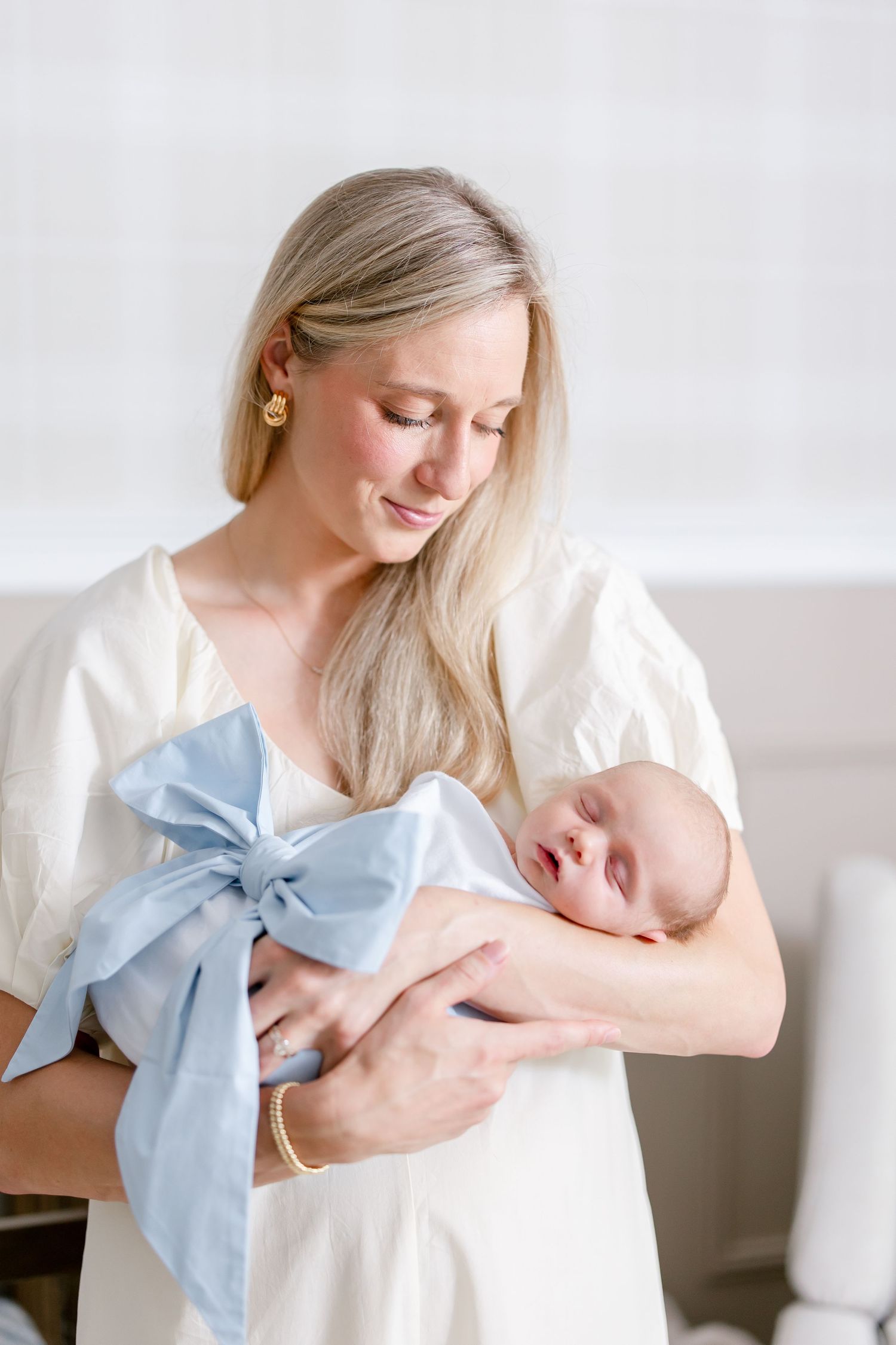 A tender moment as a parent cradles a newborn baby wrapped in a blue bow against a light neutral background.