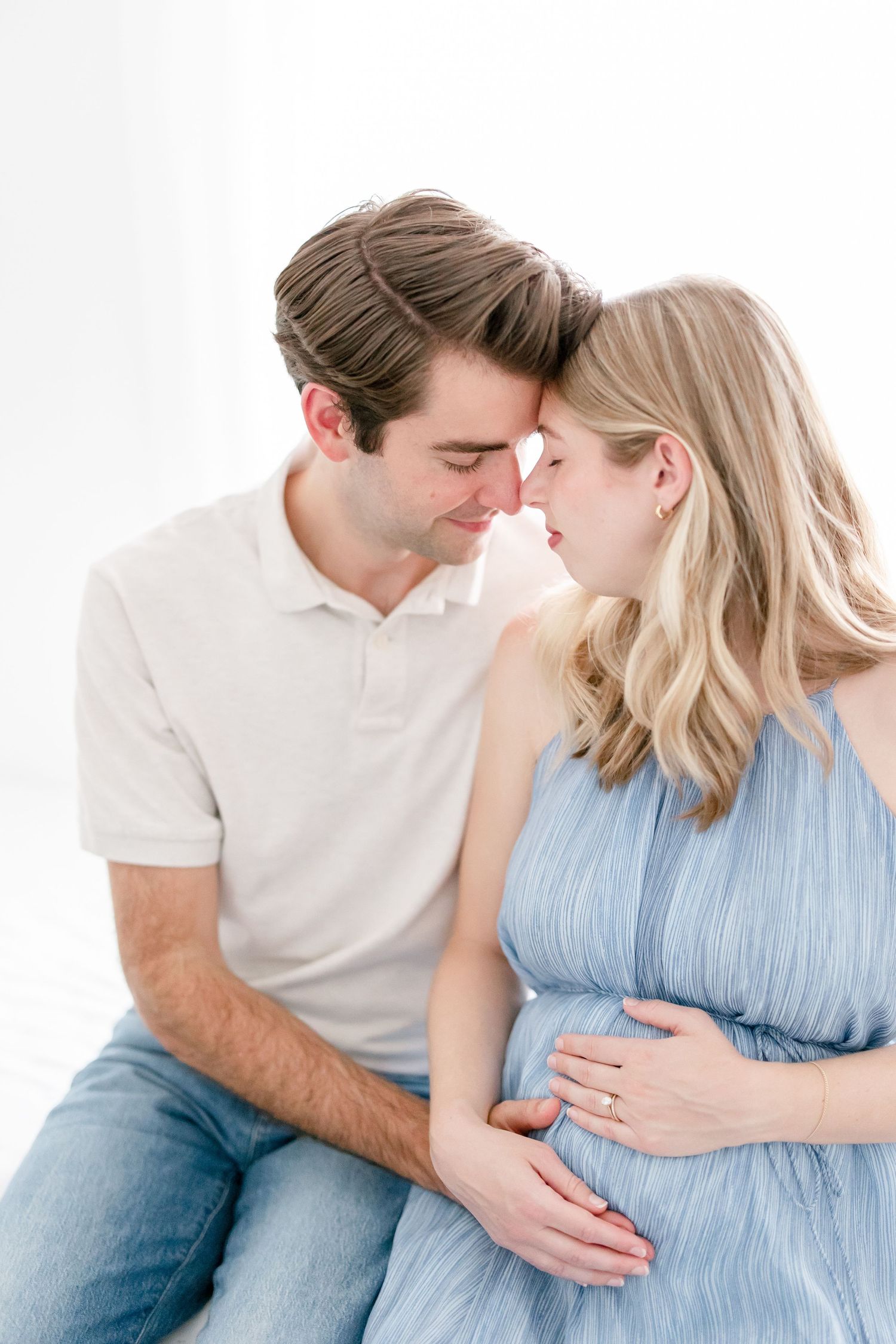 A couple in white and blue attire share intimate moments while focusing on her pregnant belly.