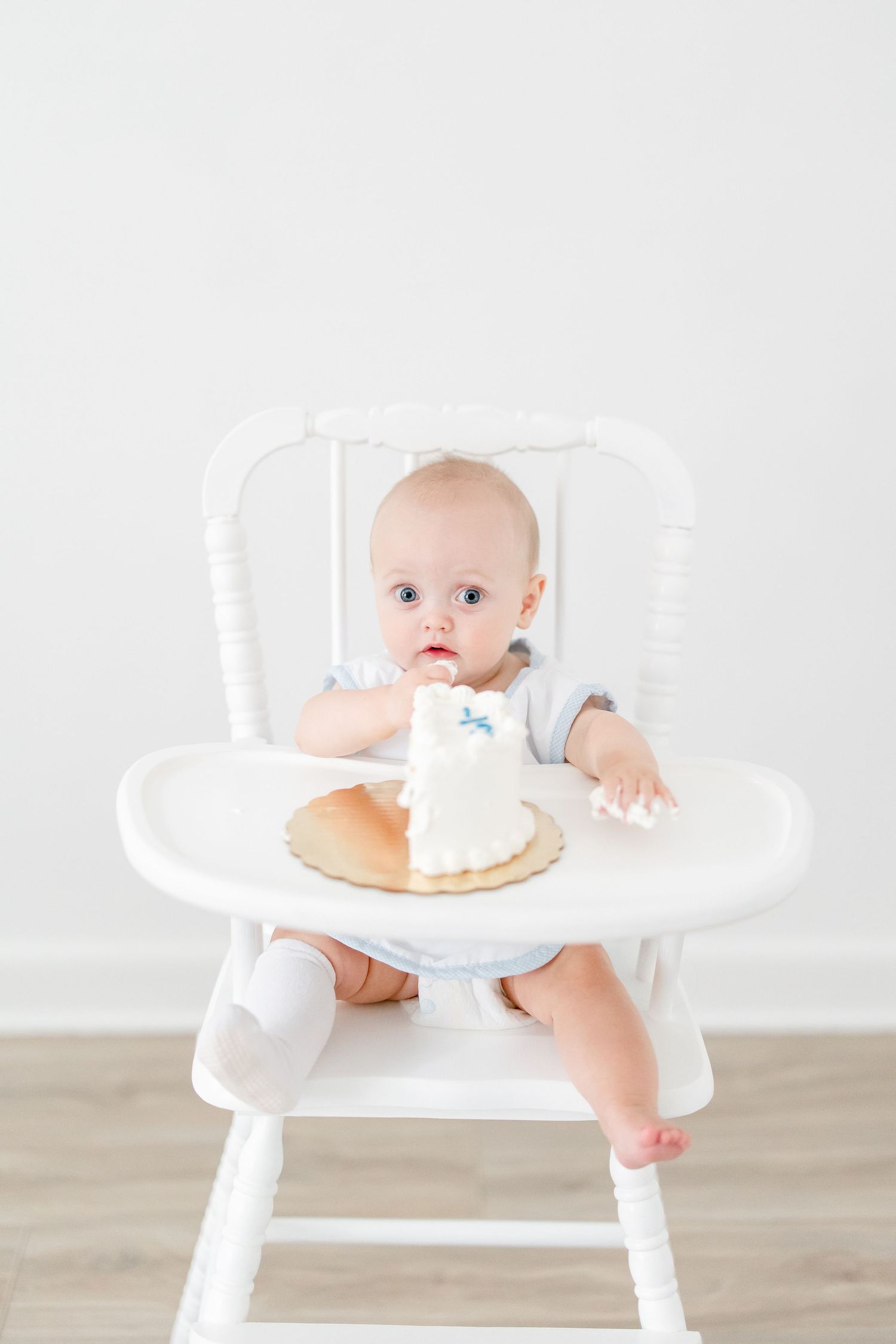 Baby sits in white high chair with small cake for first birthday celebration.