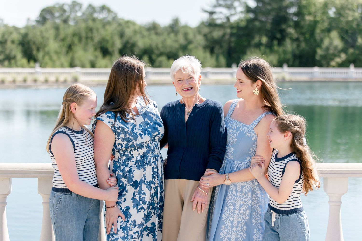 A group enjoys a sunny afternoon together by a serene lake with trees and landscaping in the background.