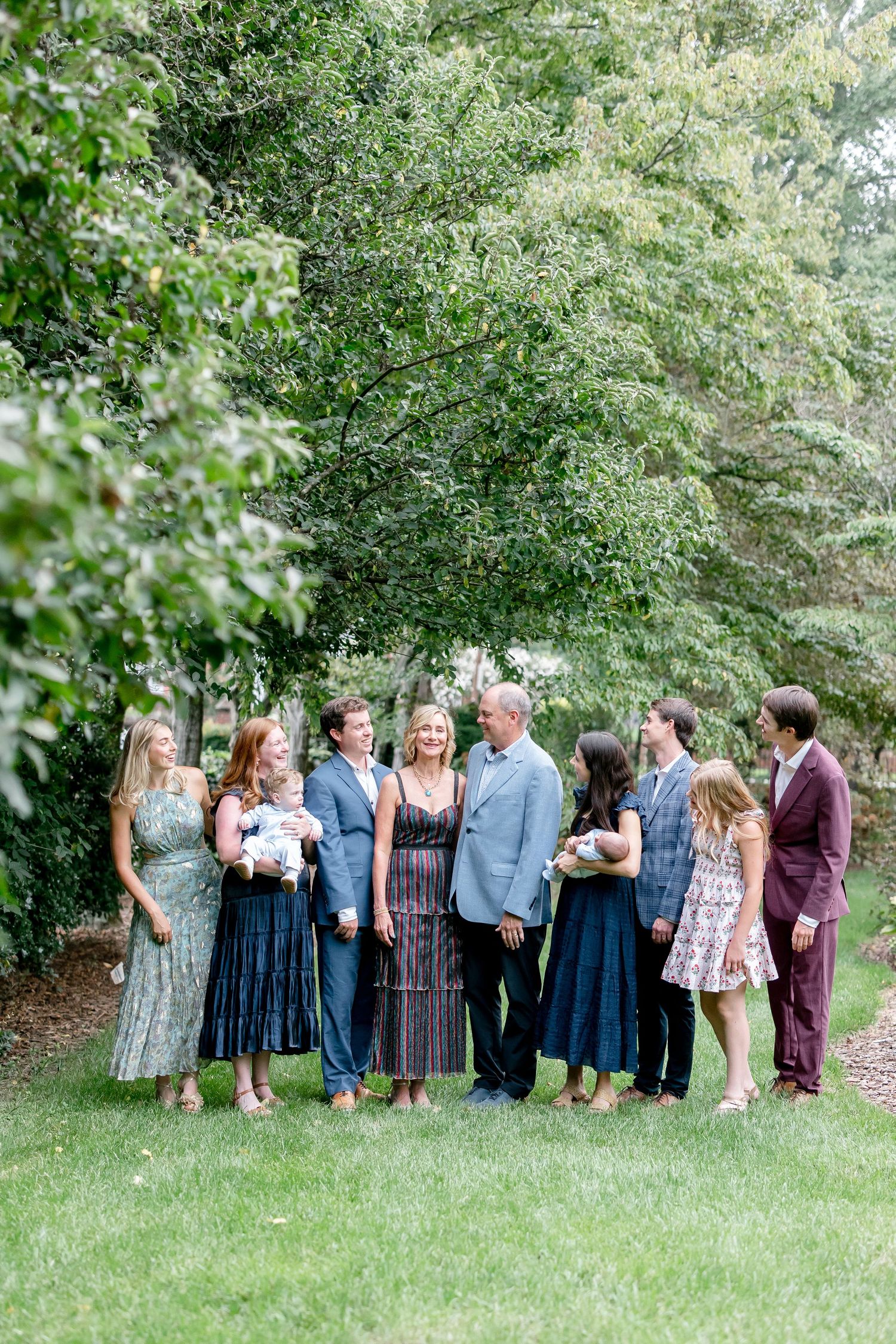 A group in coordinated blue and floral outfits poses together under lush green trees on a summer day.