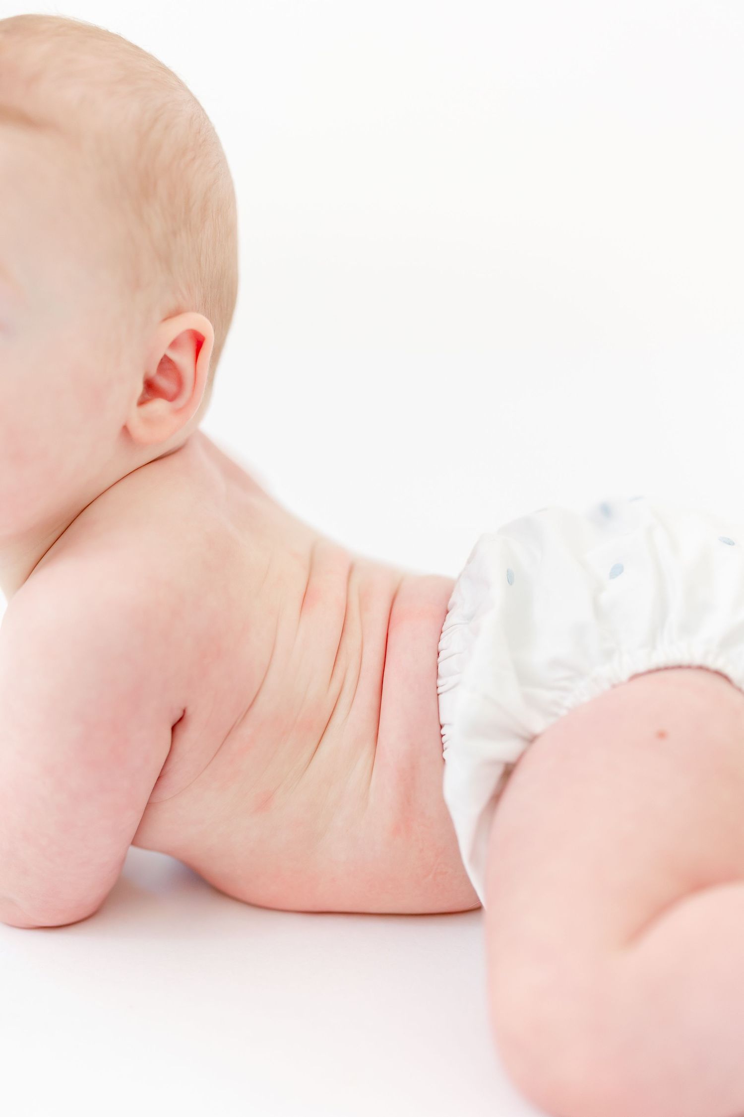 Baby in a white diaper lying on their tummy with head turned to the side against a clean white background.