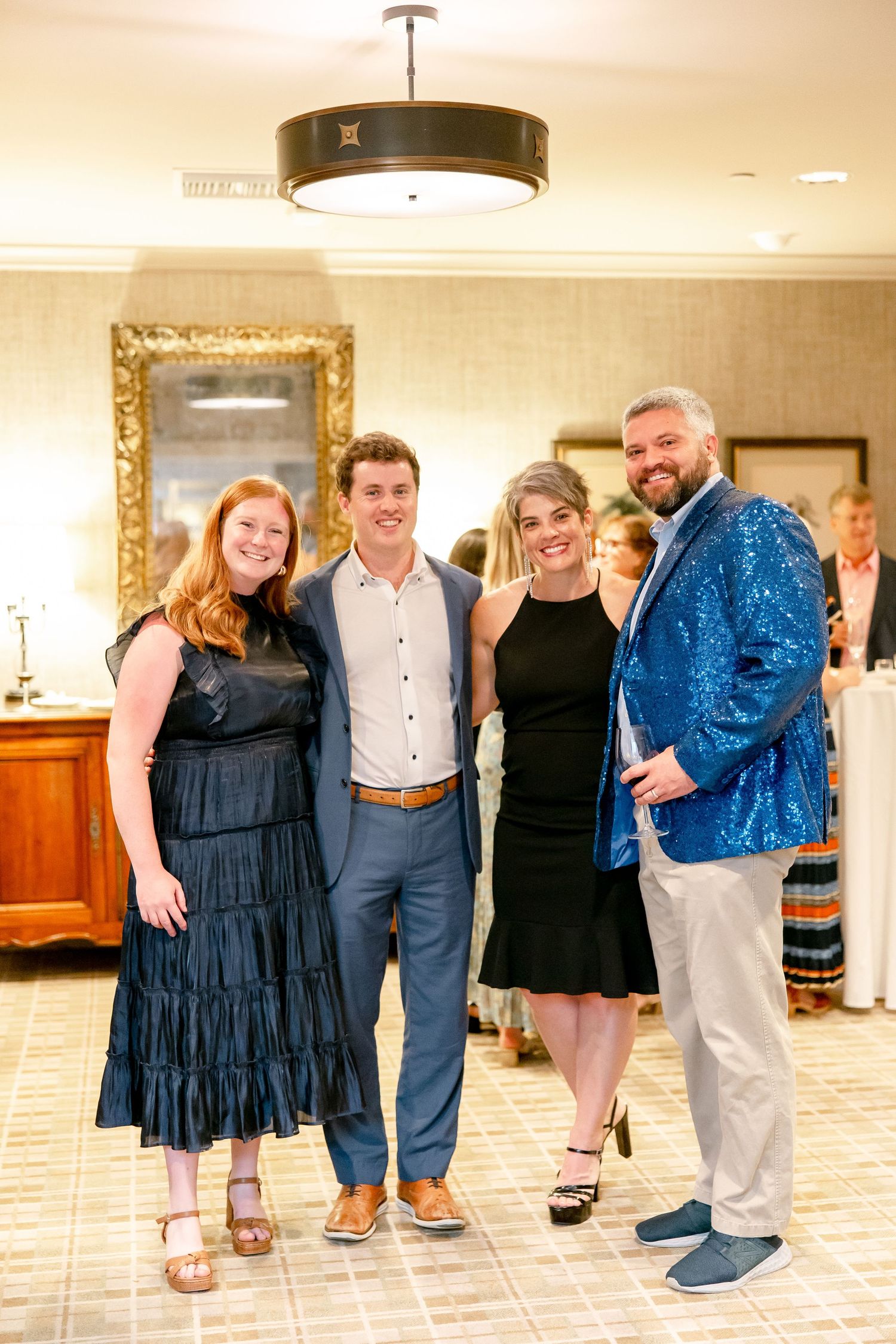 Group photo of people in formal attire posing together in an indoor venue with tiled flooring.