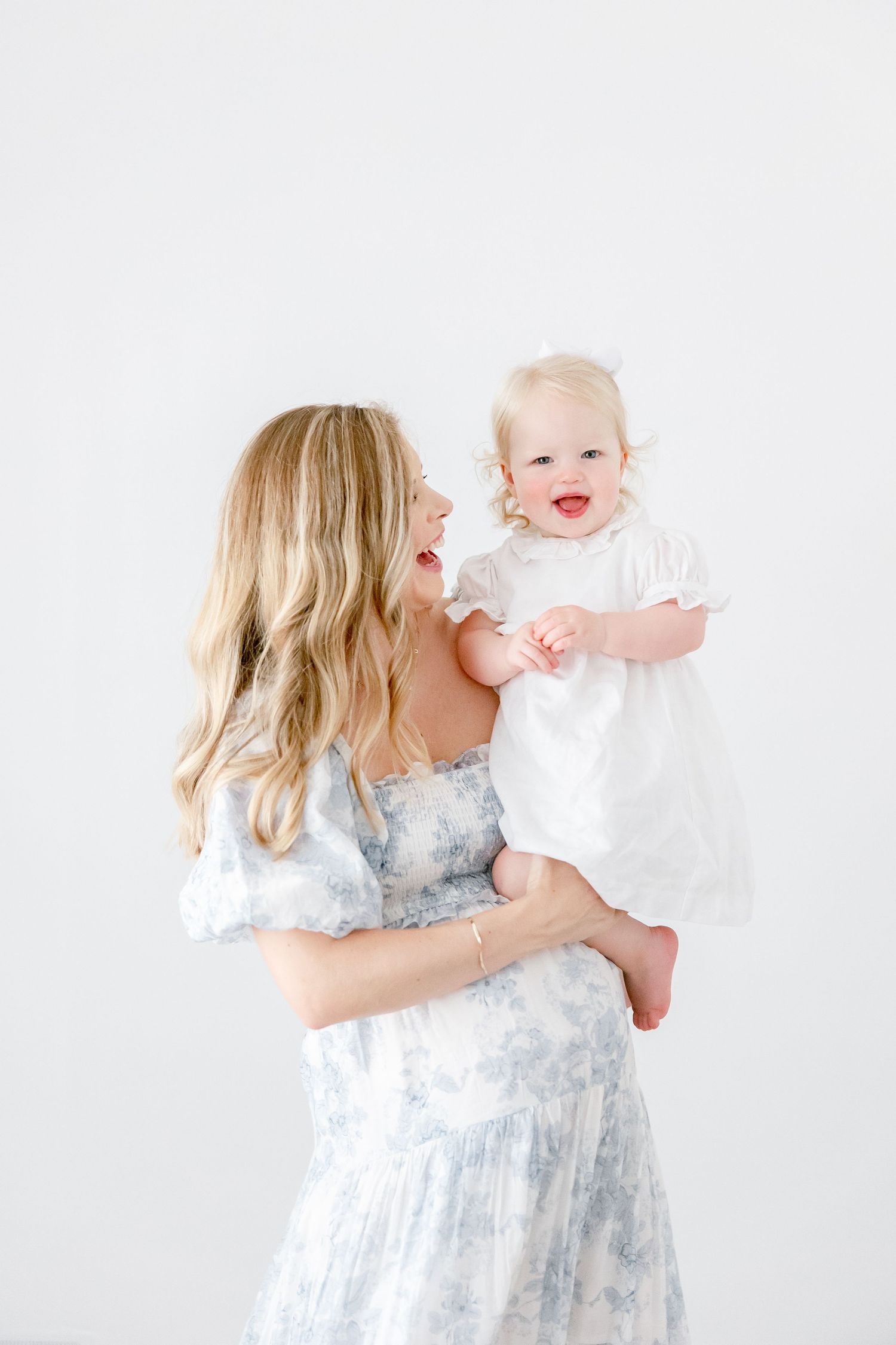 A tender motherhood moment captured in a bright white studio setting with matching white dresses.