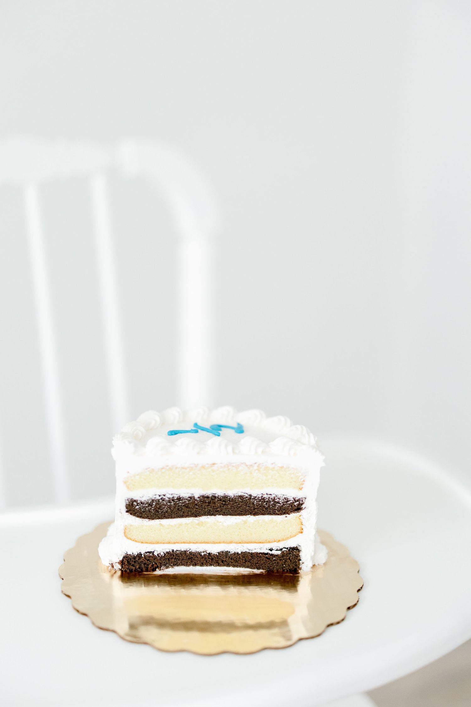 A sliced white frosted cake with chocolate layers displayed on a gold cake board.