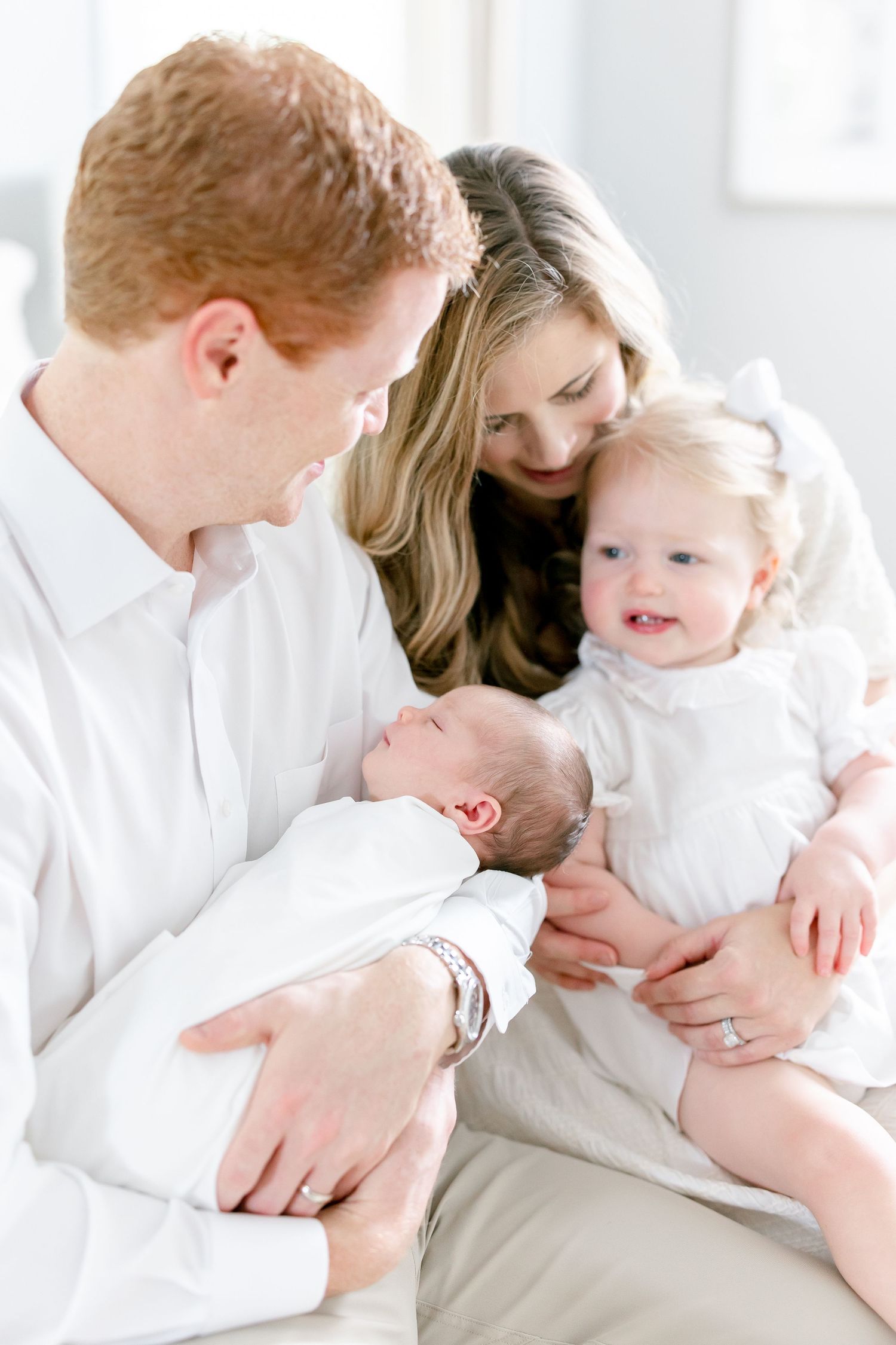 Intimate family moment captured in bright white room with parents and young children.