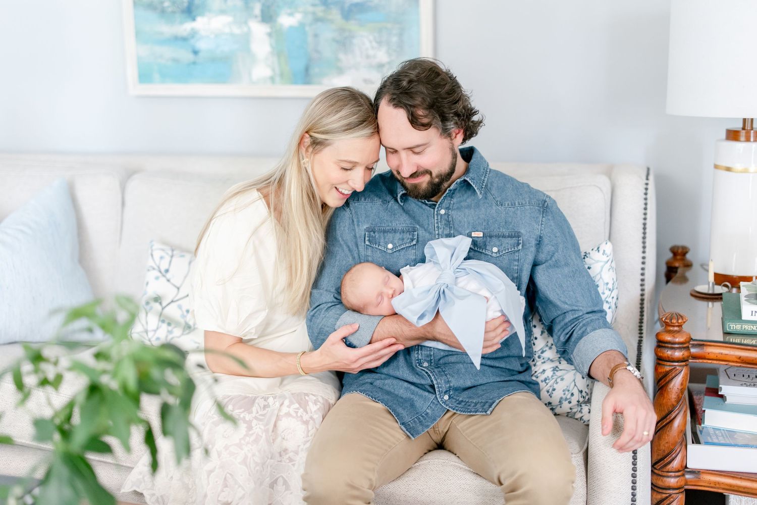 Parents sharing intimate moment with newborn baby on couch beneath blue wall art.