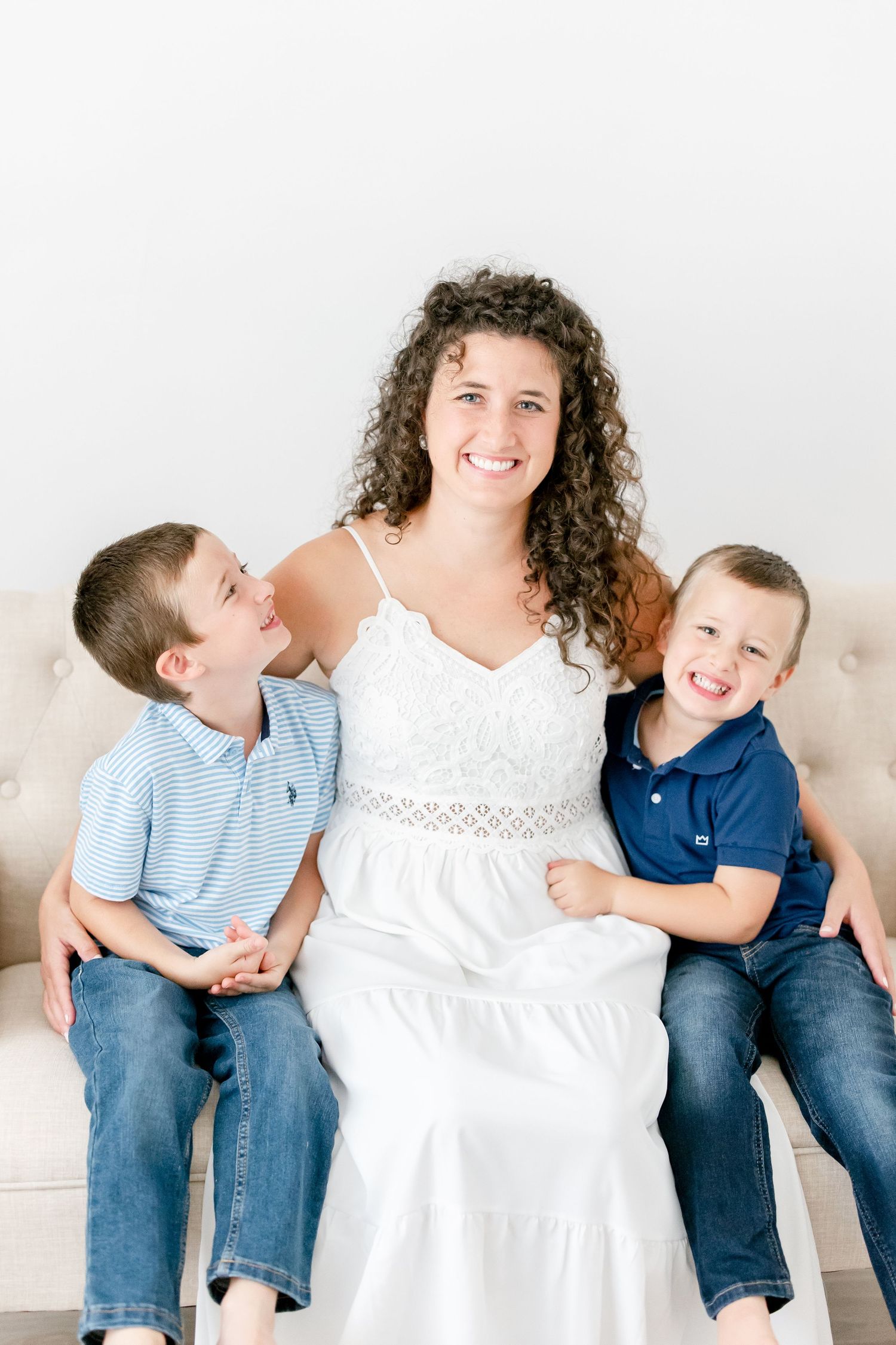 Family dressed in white and blue outfits sharing playful moments together against white background.