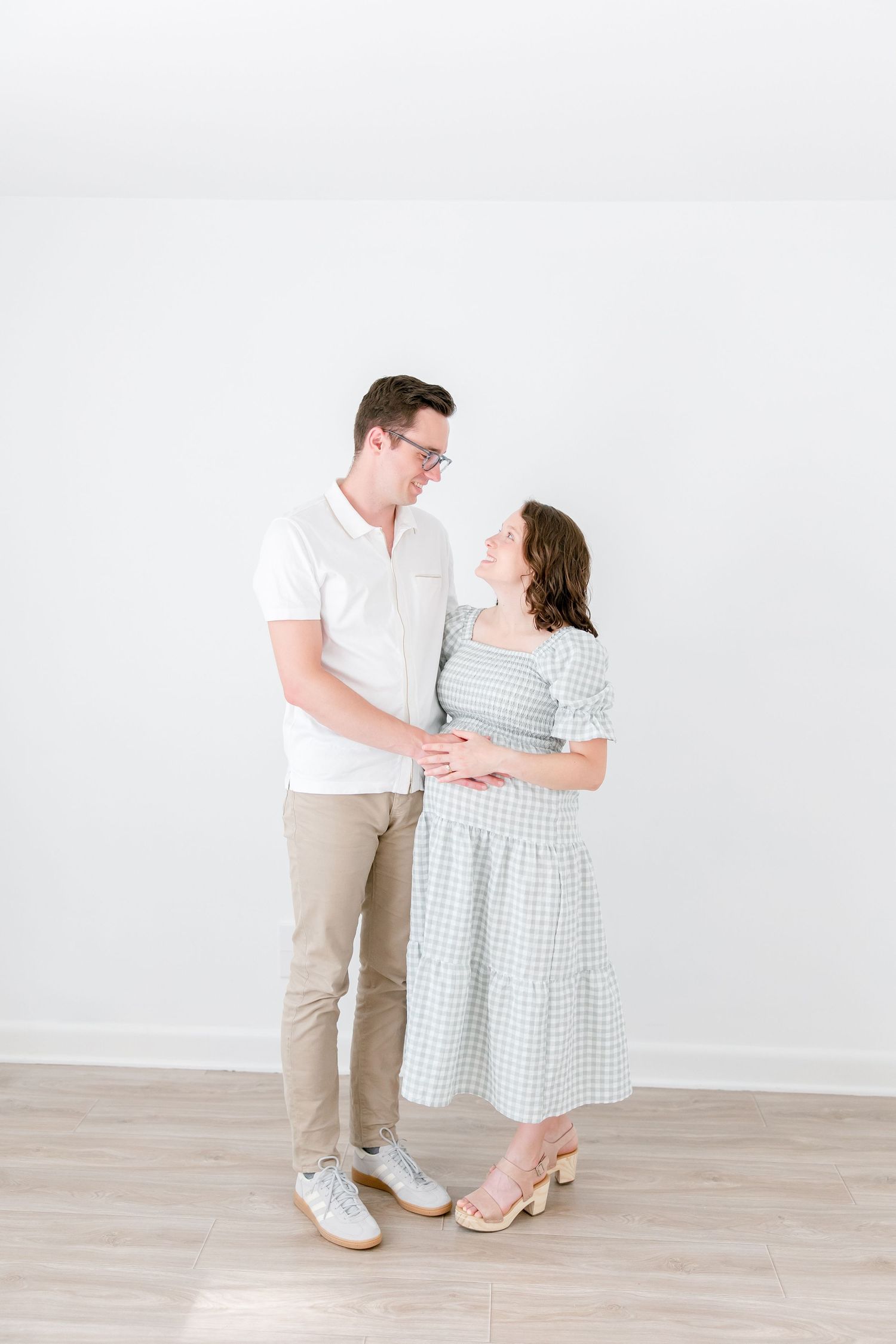A couple in white and blue outfits share tender romantic moments while posing against a light-colored backdrop.