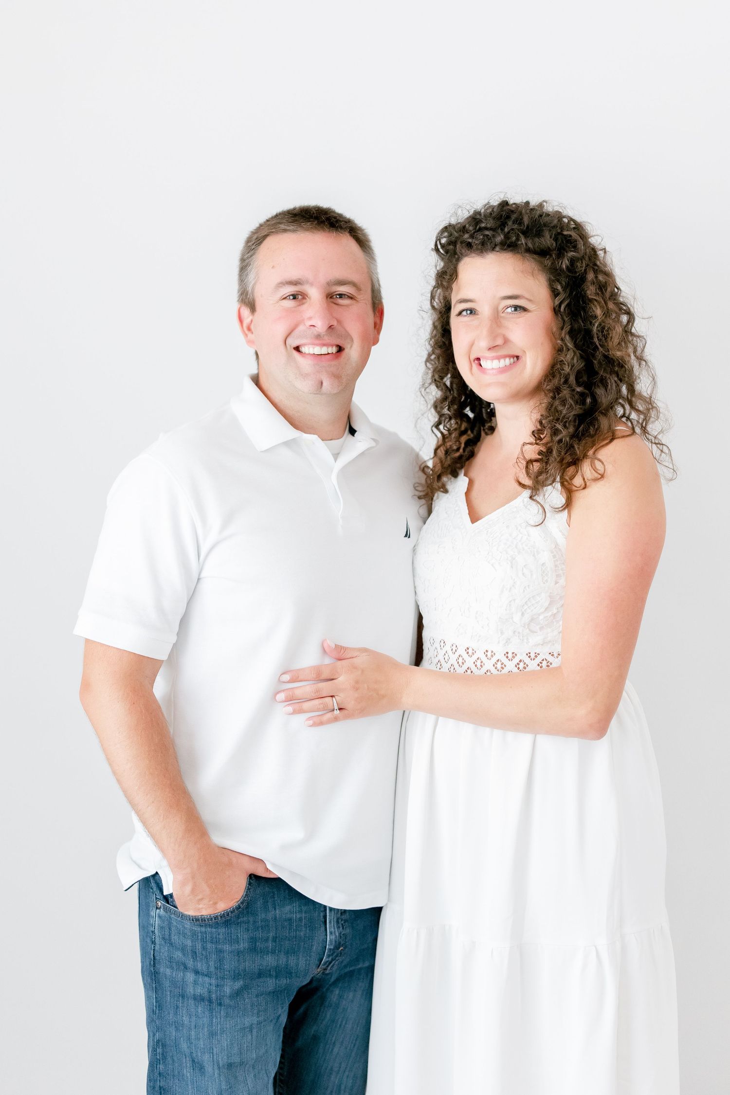 Couple in coordinated white outfits embracing and laughing during indoor photo session.