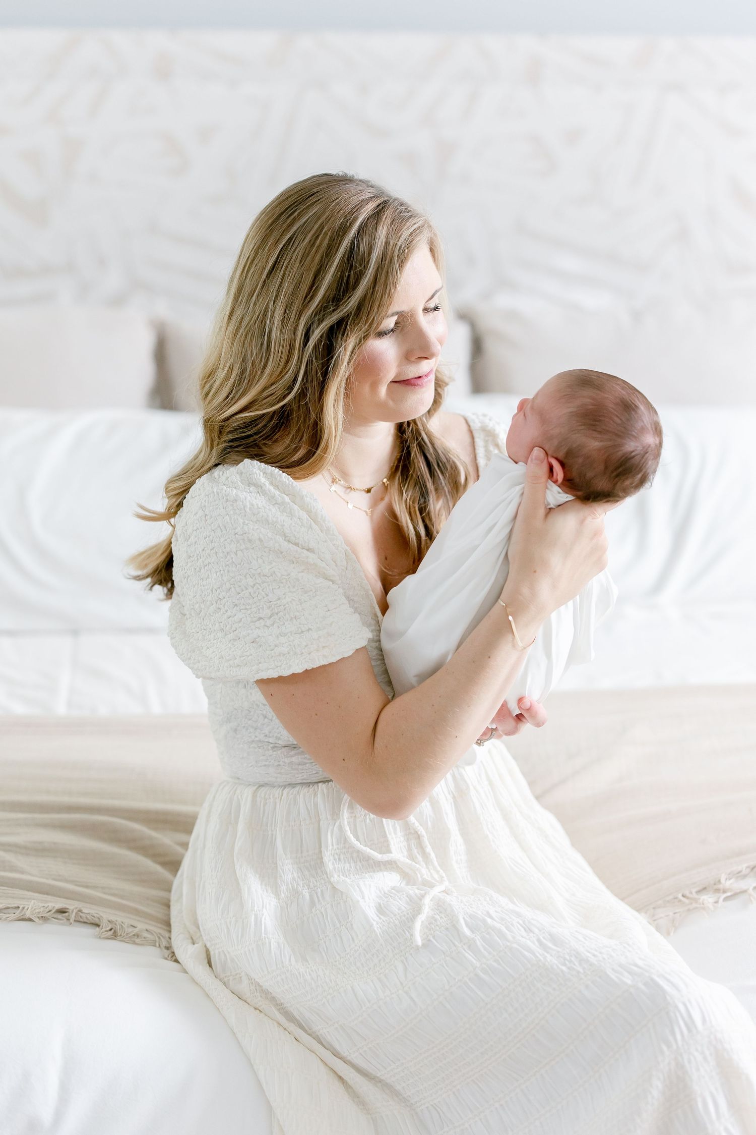 A tender moment between parent and child captured in soft white tones on a bed.