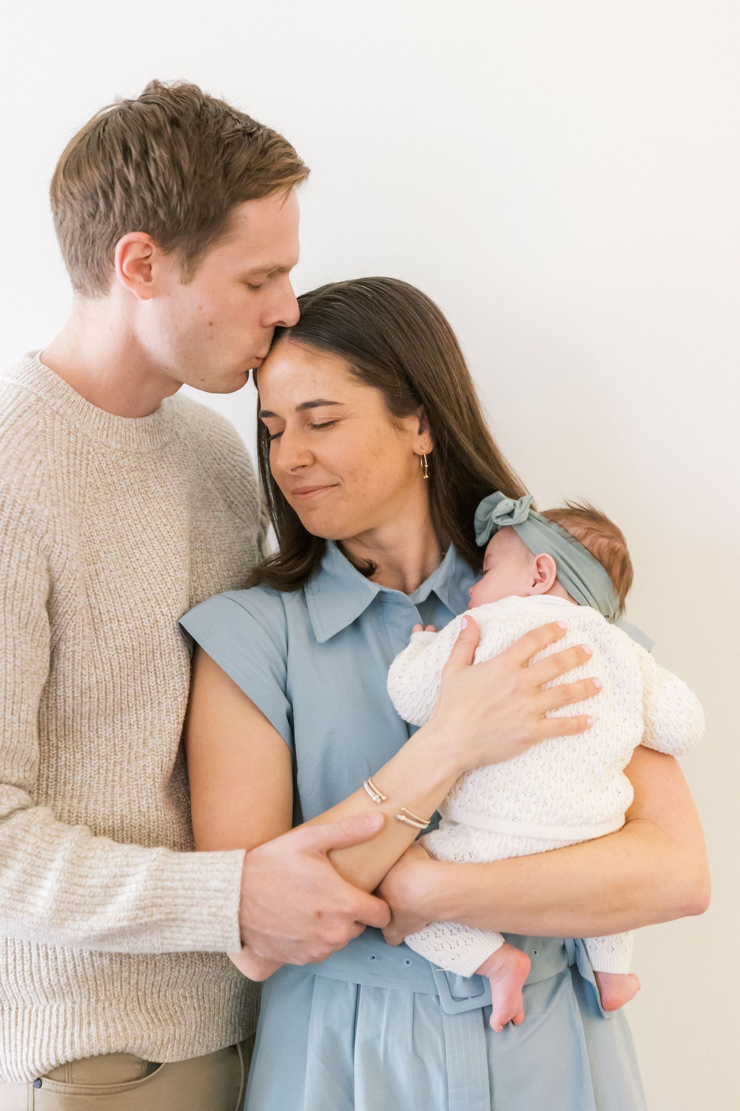 Intimate family moment with new parents embracing their swaddled newborn.