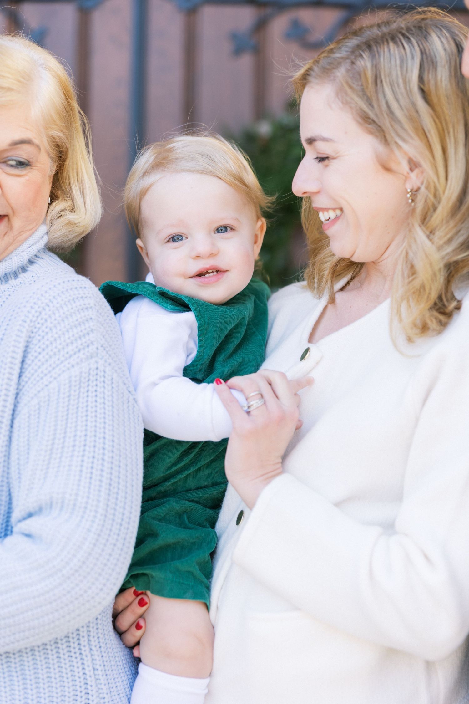 Three generations share a joyful moment together outdoors, wearing cozy winter whites and emerald green.