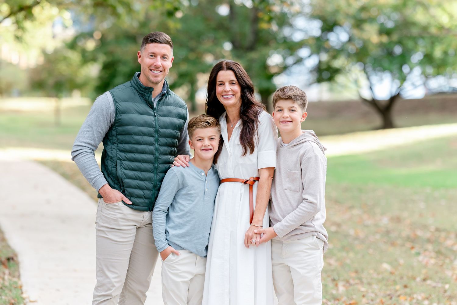 A family in coordinating neutral outfits poses together outdoors during a fall photo session.