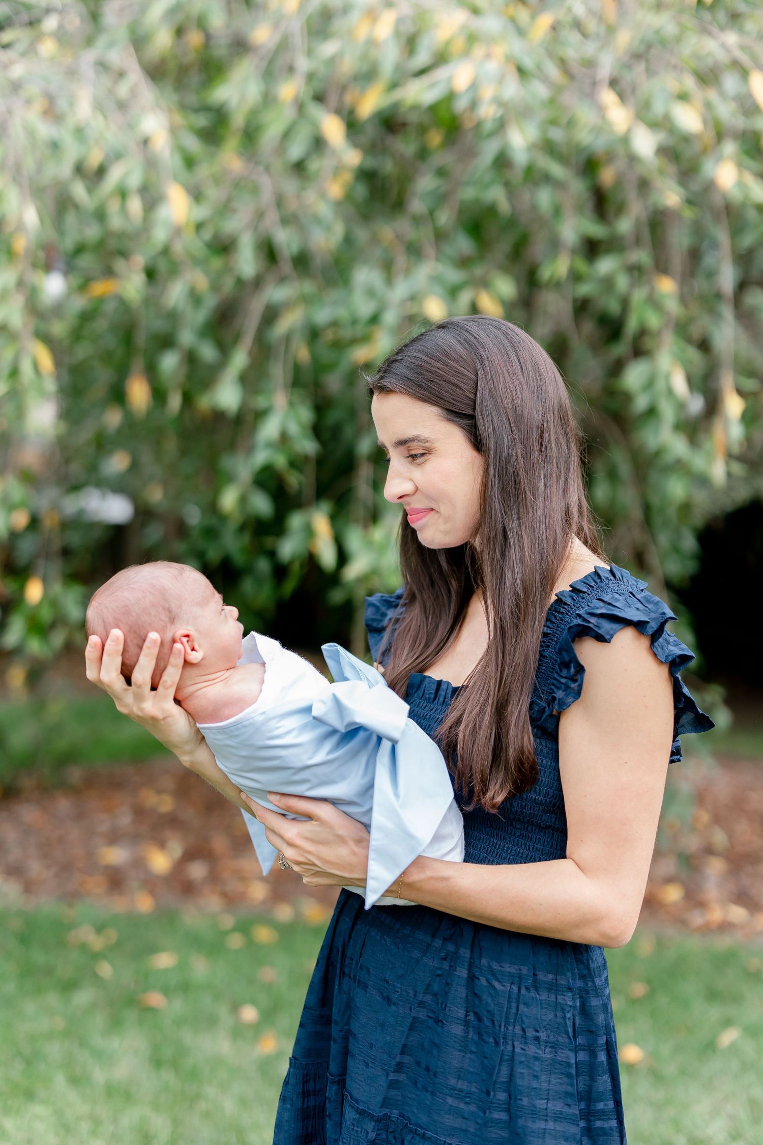 Woman in navy dress holding newborn baby in garden setting.