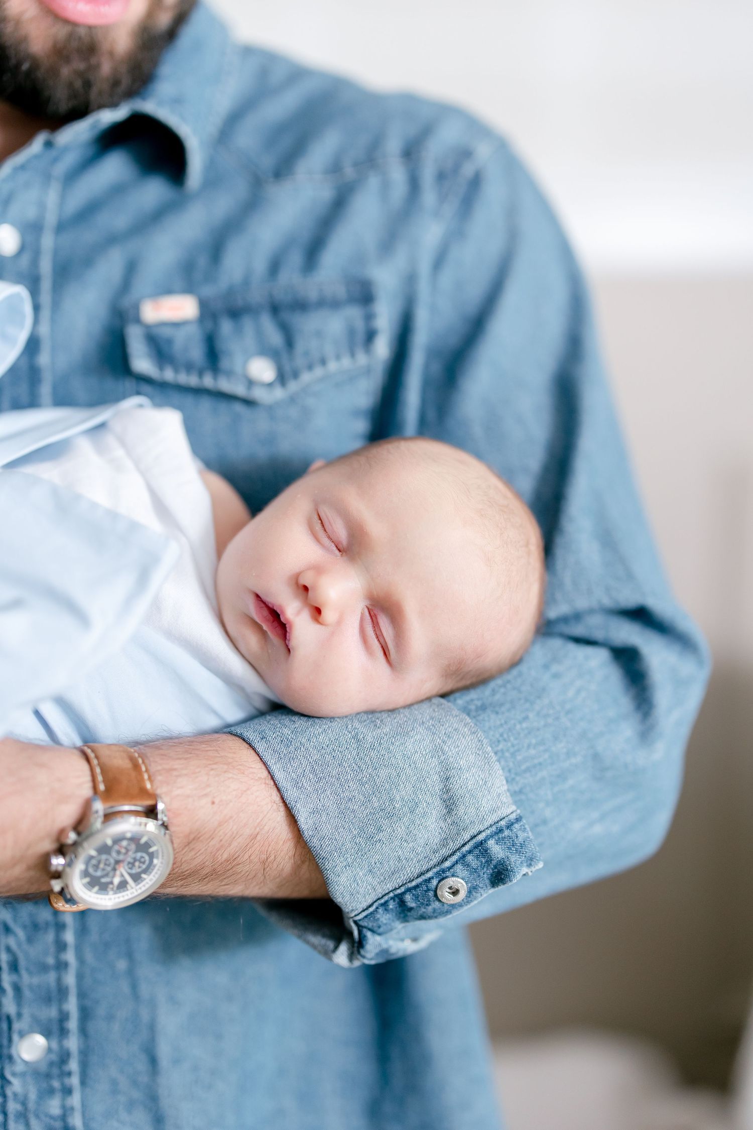 A sleeping newborn baby cradled in denim-clad arms.