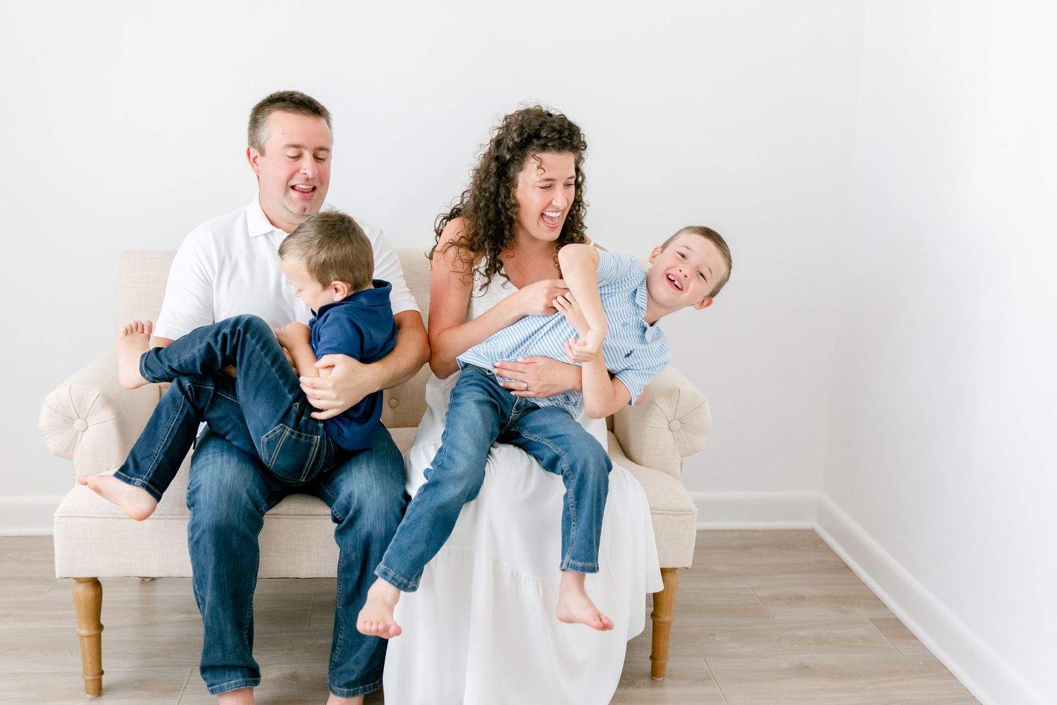 A sweet family bonding moment captured on a white sofa in a light, airy setting.