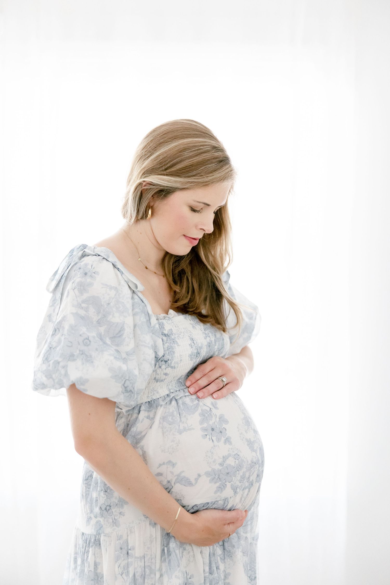 Elegant maternity portraits featuring a woman in a delicate blue and white floral dress against white background.