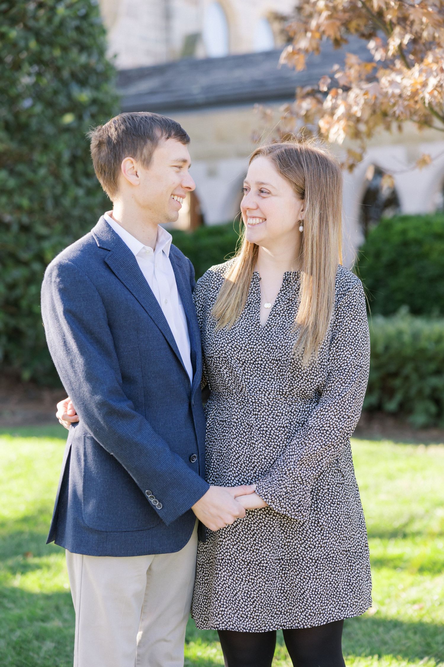 A couple shares a loving moment on a sunny day outside a stone building with green ivy.