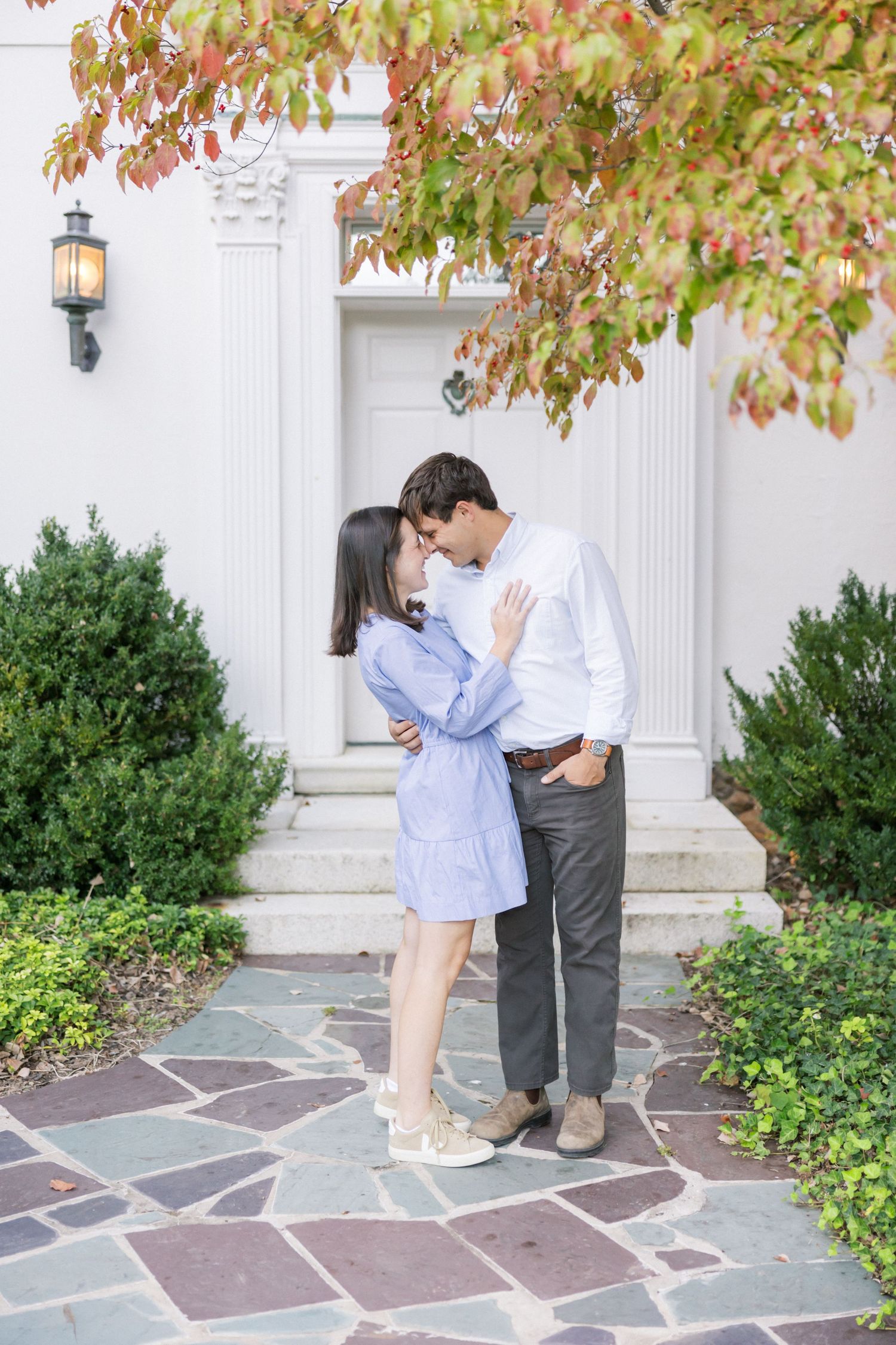 A romantic moment on a stone patio with autumn leaves and white columns framing the entrance of an elegant building.