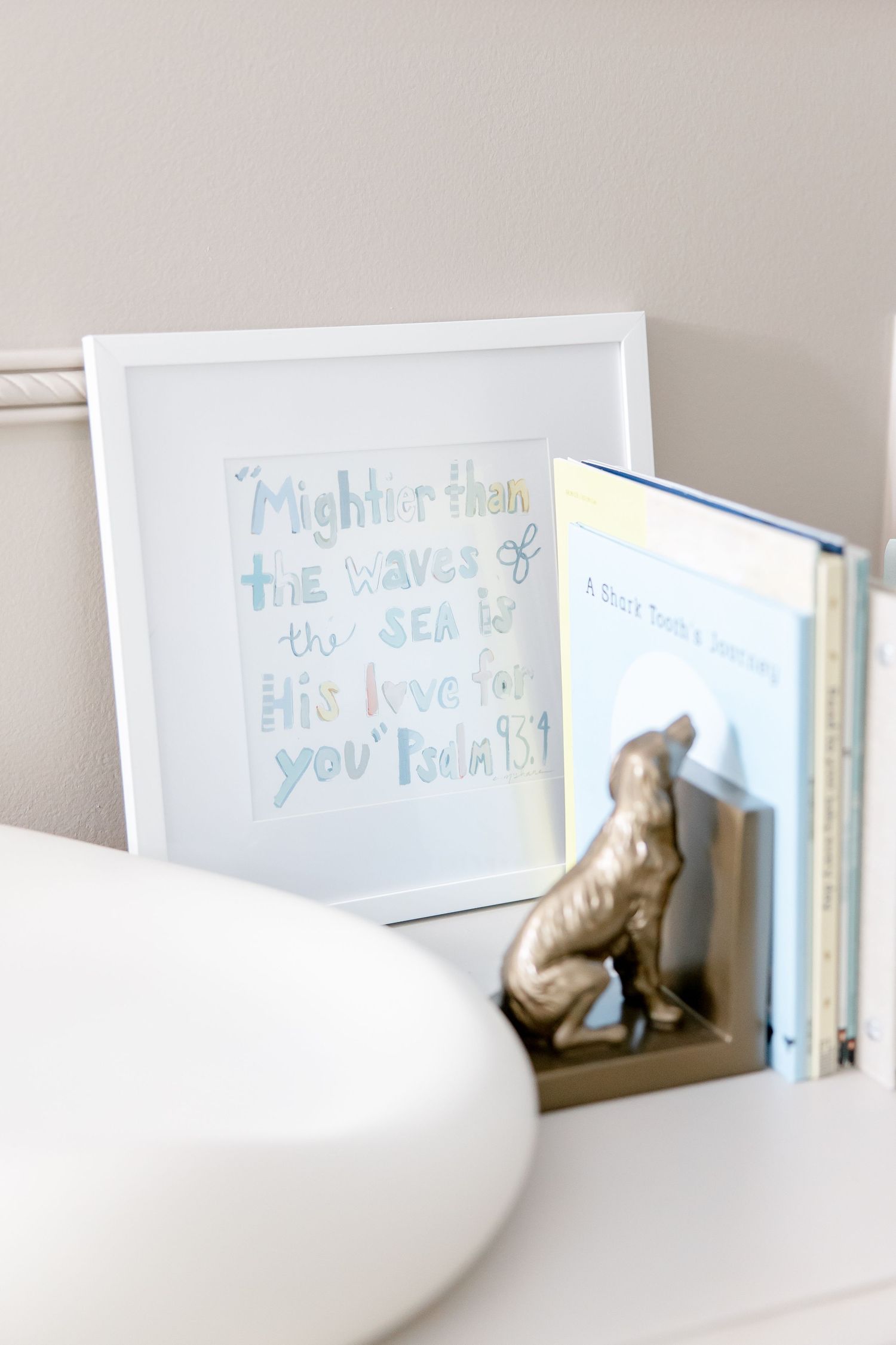 Soft blue and white nursery decor with framed artwork on shelf.